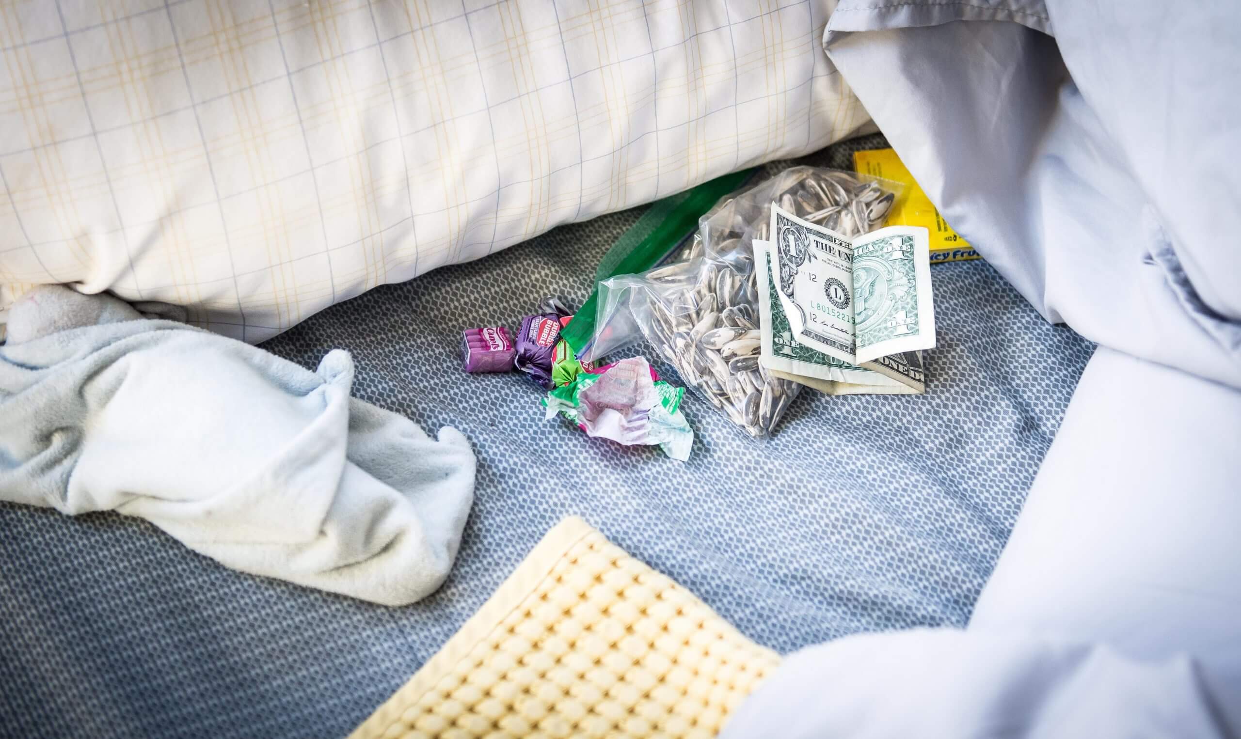 Several items on a bed include cash, candy, and a bag of sunflower seeds.