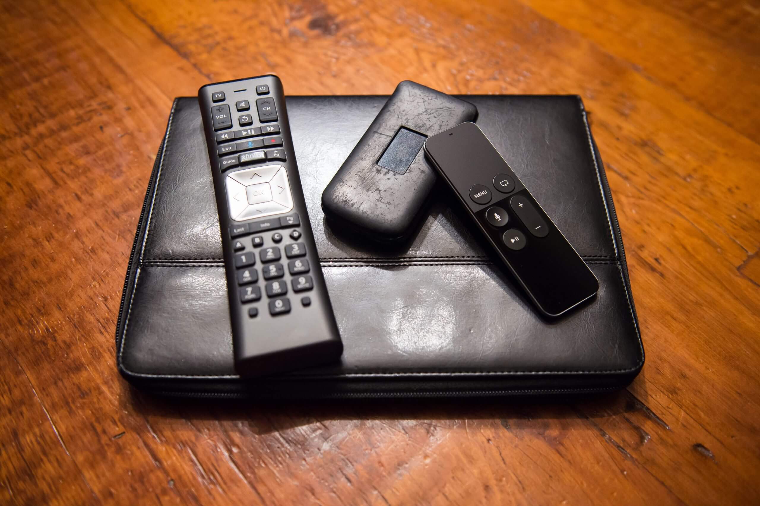 Remotes and an electronic device are on top of a leather binder.