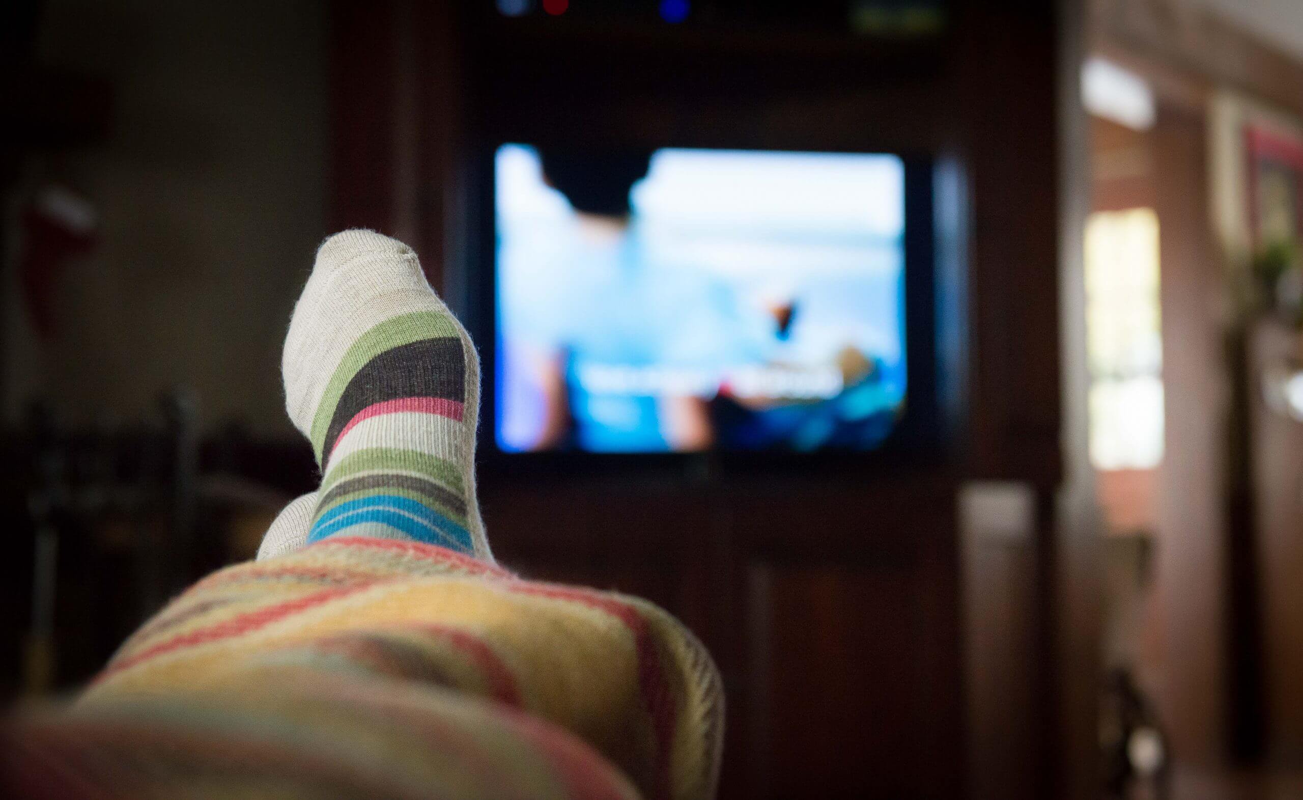 A focused view of a person's feet up with an unfocused view of a television screen.