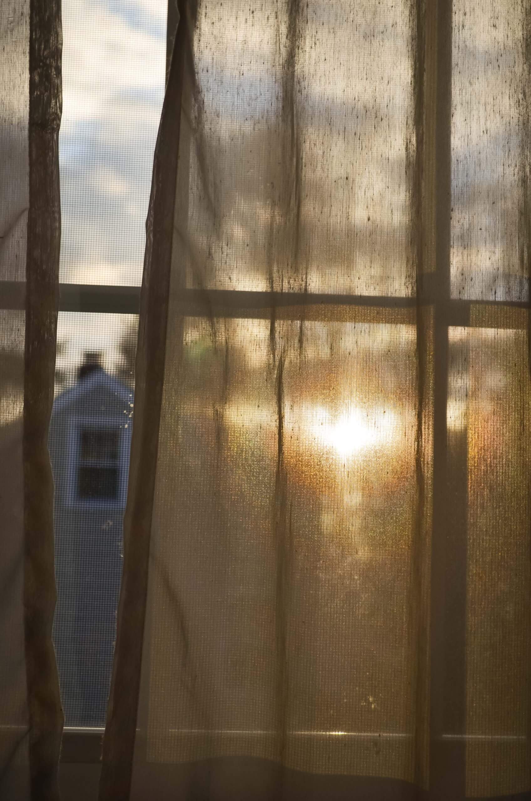 A curtain is drawn over a window. Sun shines through the curtain.
