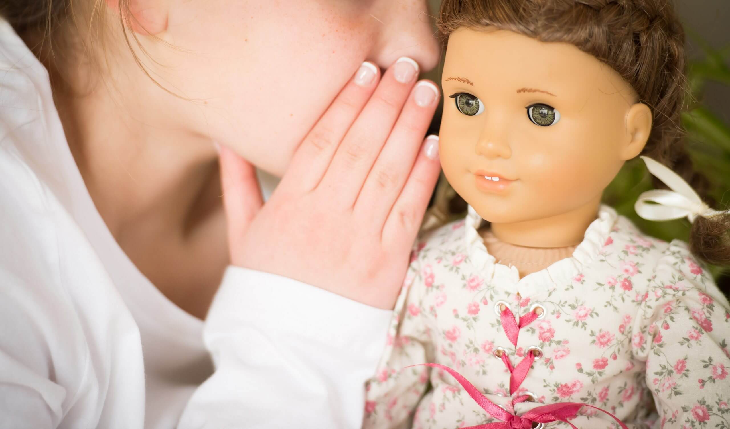 A girl whispers in the ear of a doll.