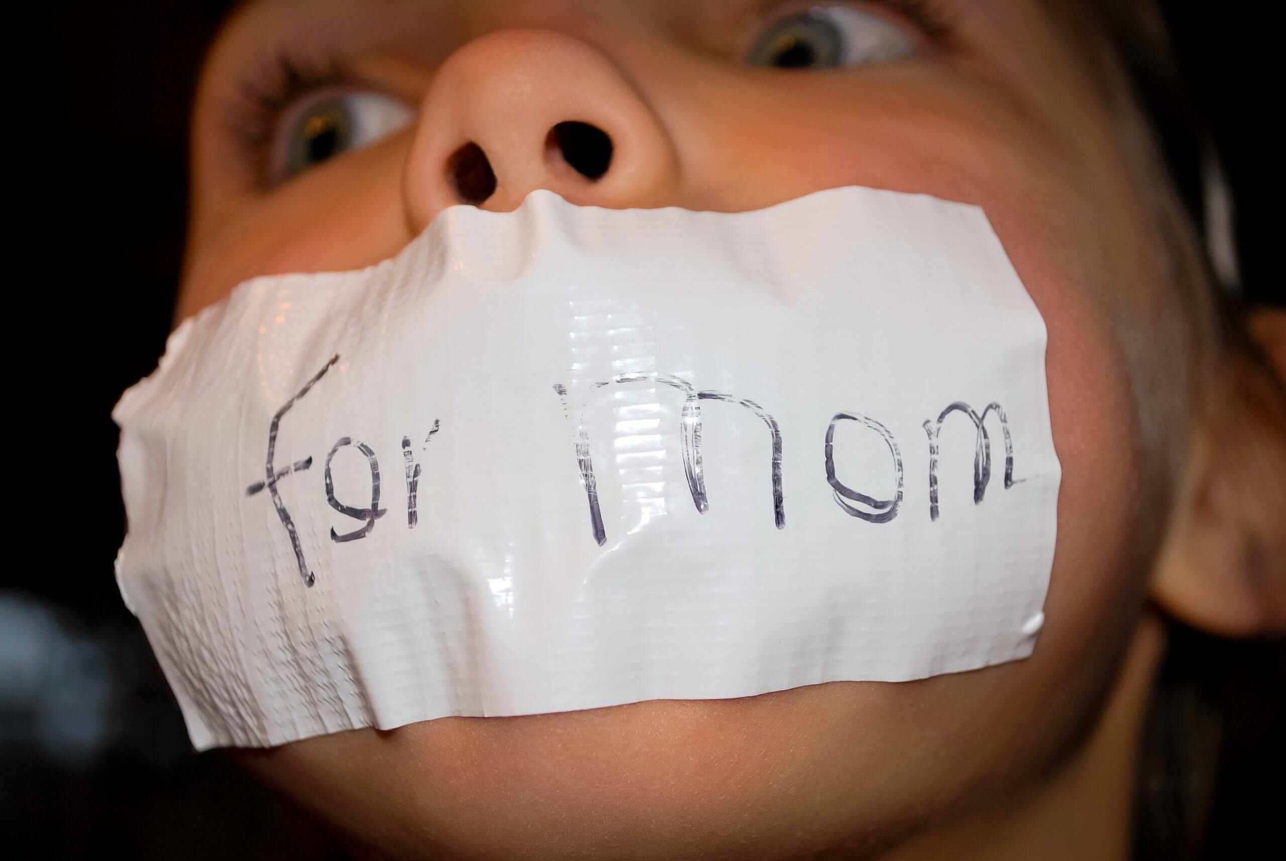 A child with duct tape covering their mouth. The duct tape reads, 