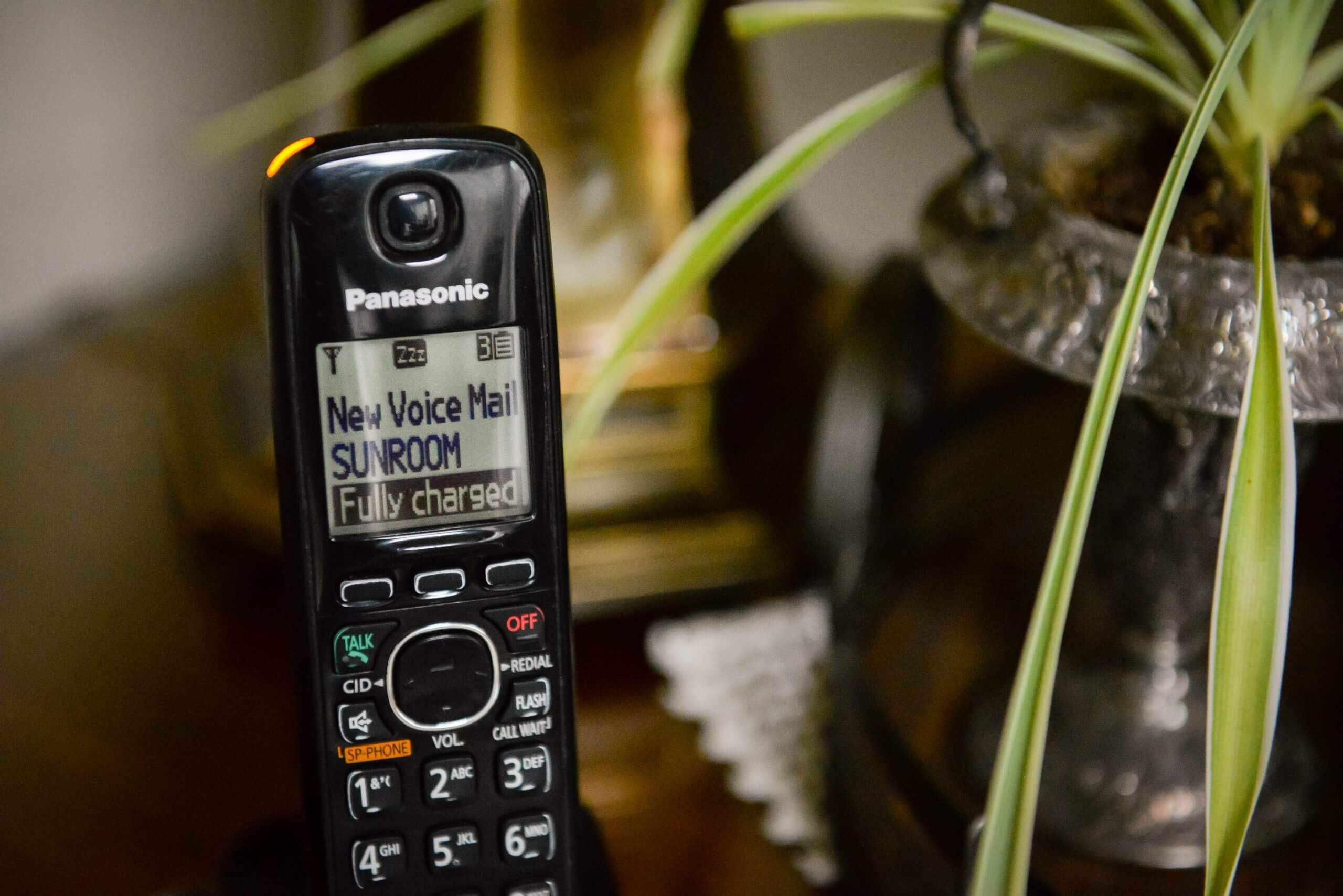 A focused view of a wireless house phone on a table. The screen of the phone reads, 