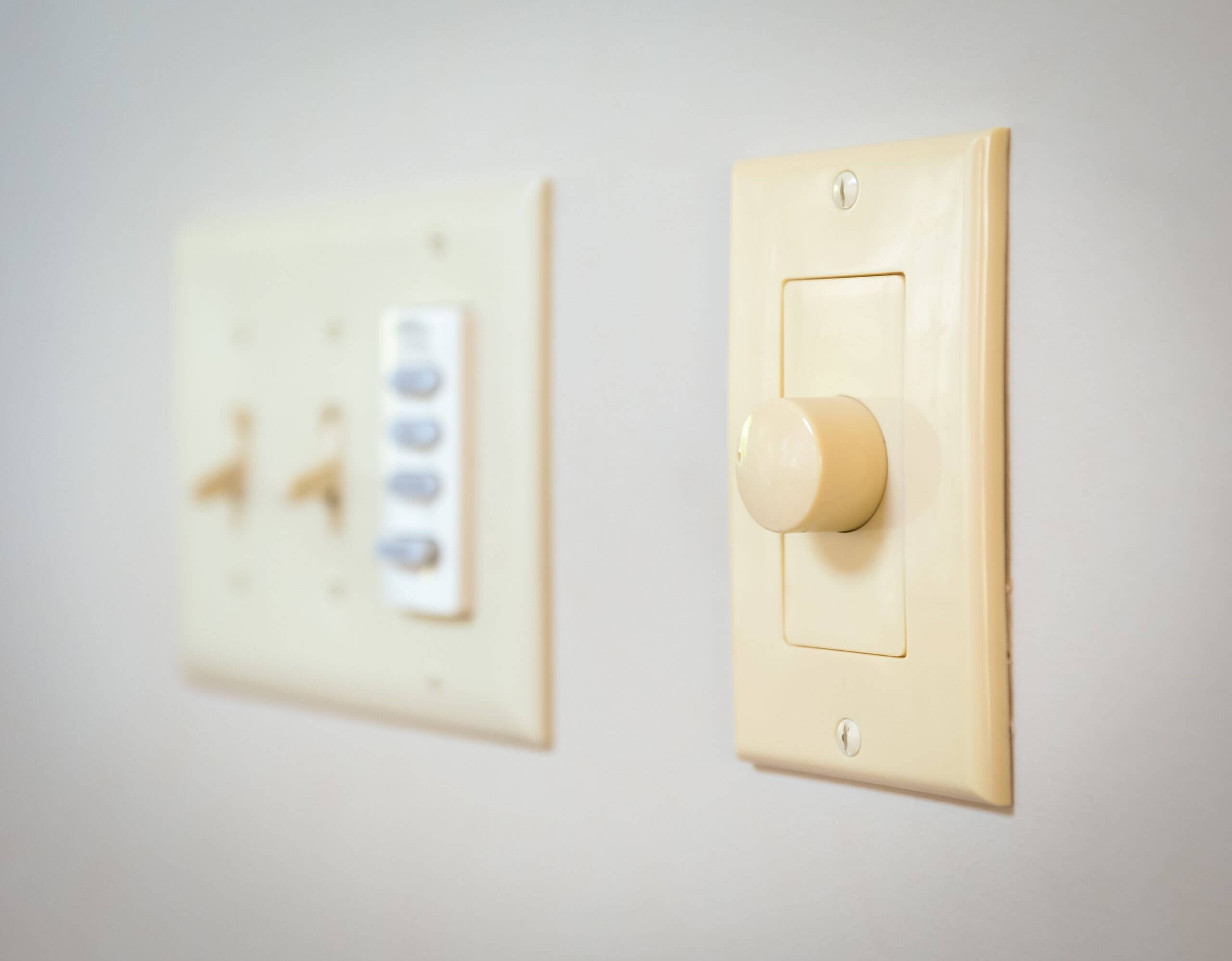 A focused view of a dimmer switch on a wall. Parallel to the dimmer switch is an unfocused view of a light switches.