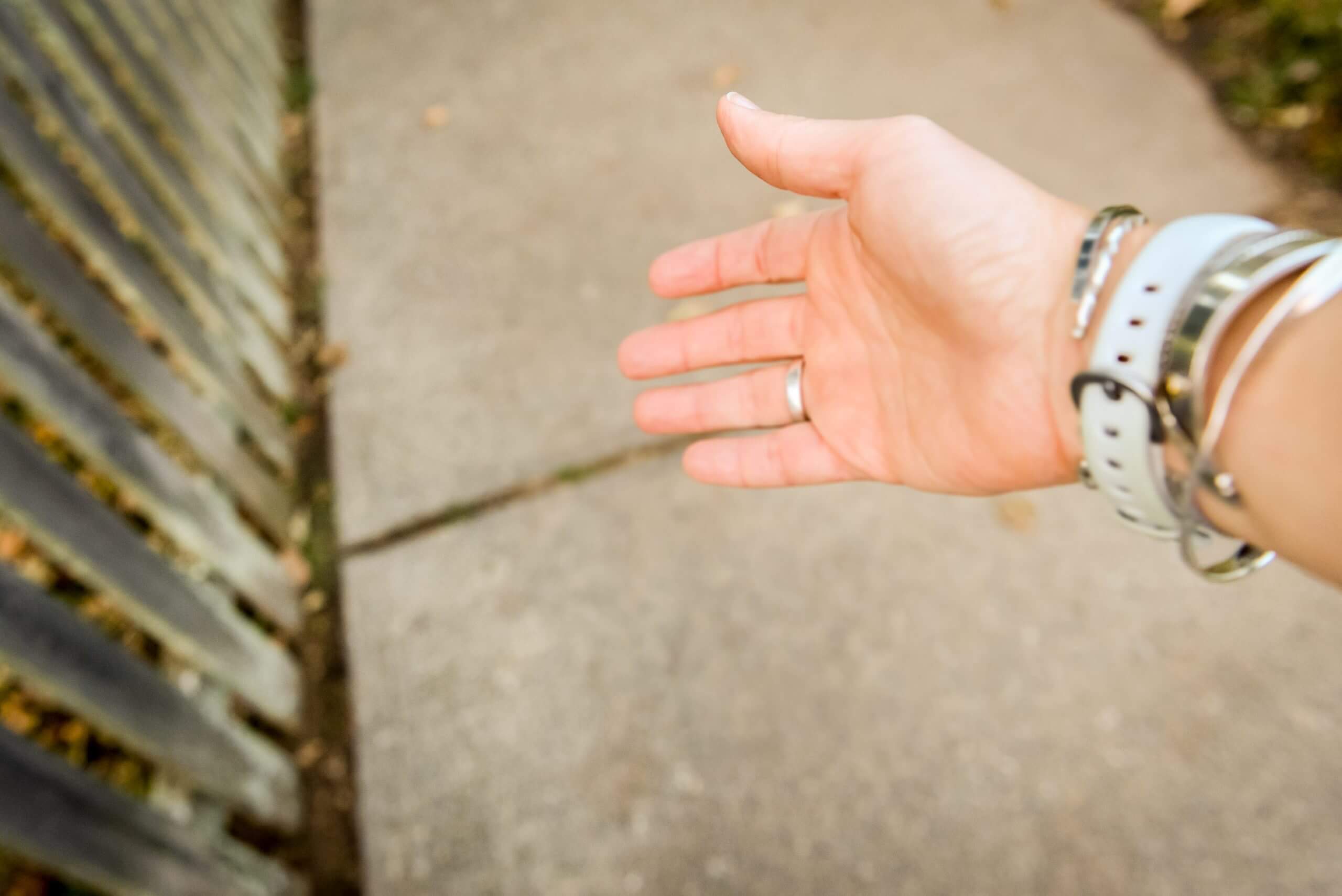A focused view of an outstretched arm and hand over an unfocused view of a sidewalk below.