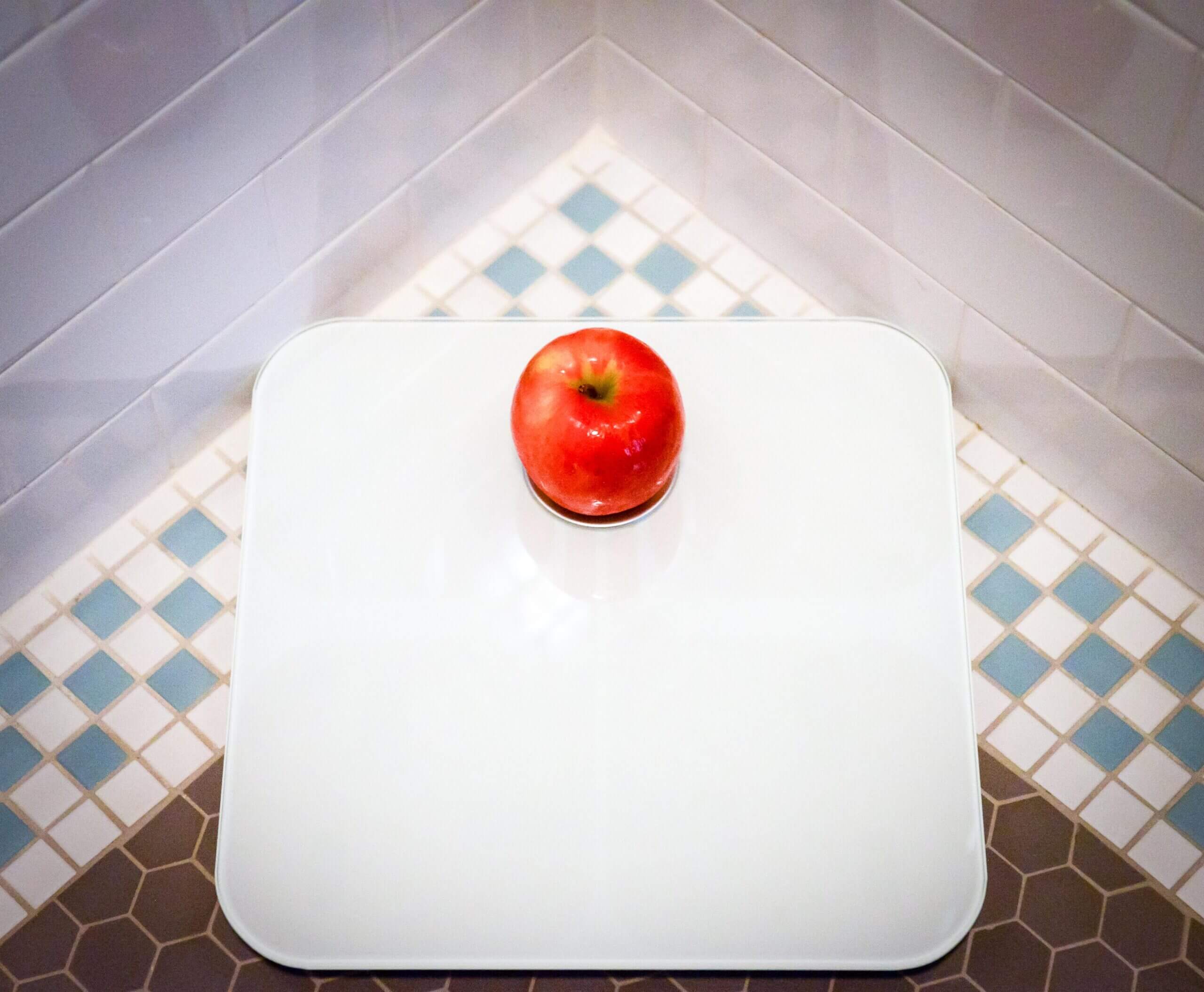 An overhead view of a bathroom scale. The screen of the scale is covered by an apple.