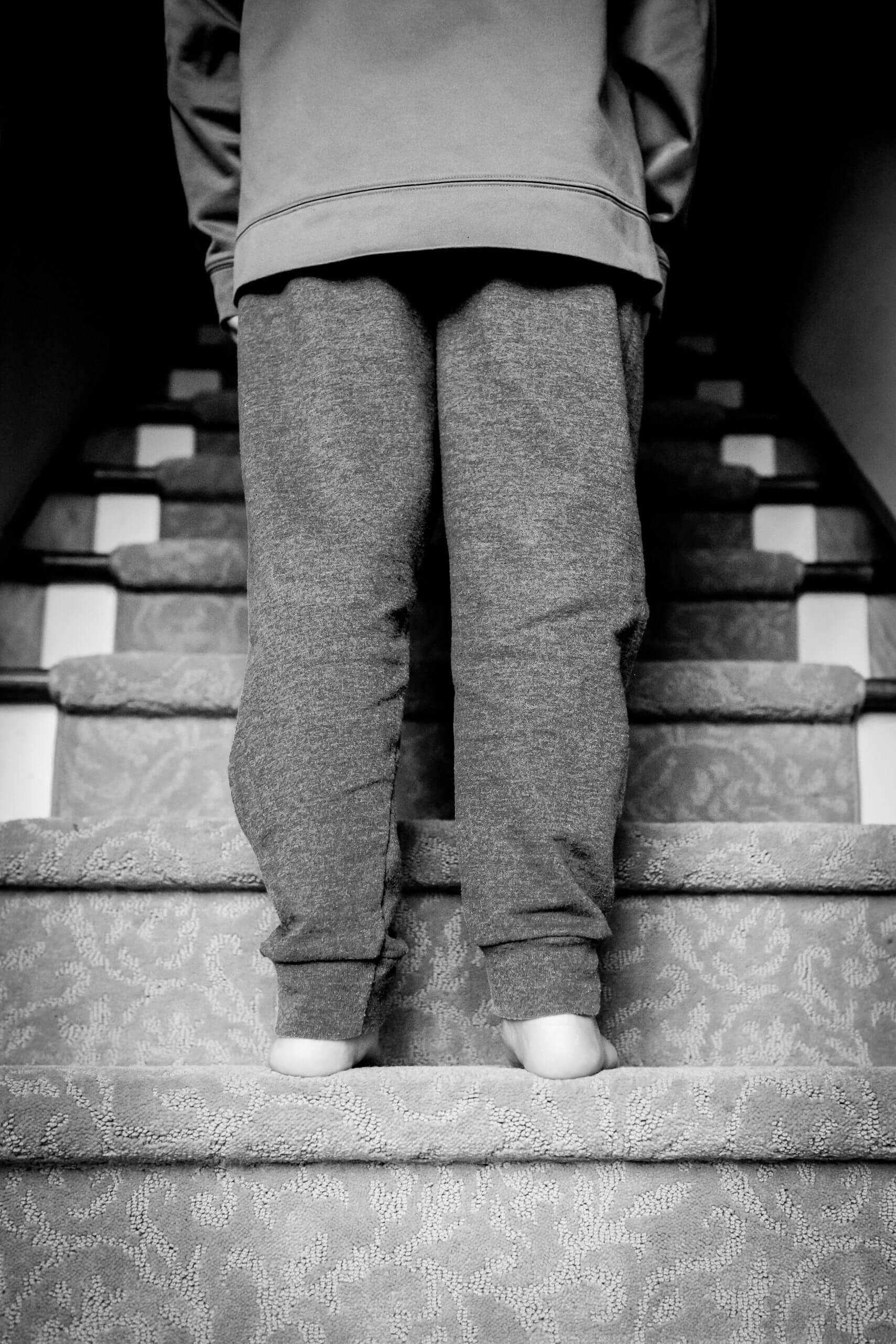 A view looking up from the bottom of the stairs shows a person wearing sweatpants standing on the second step.