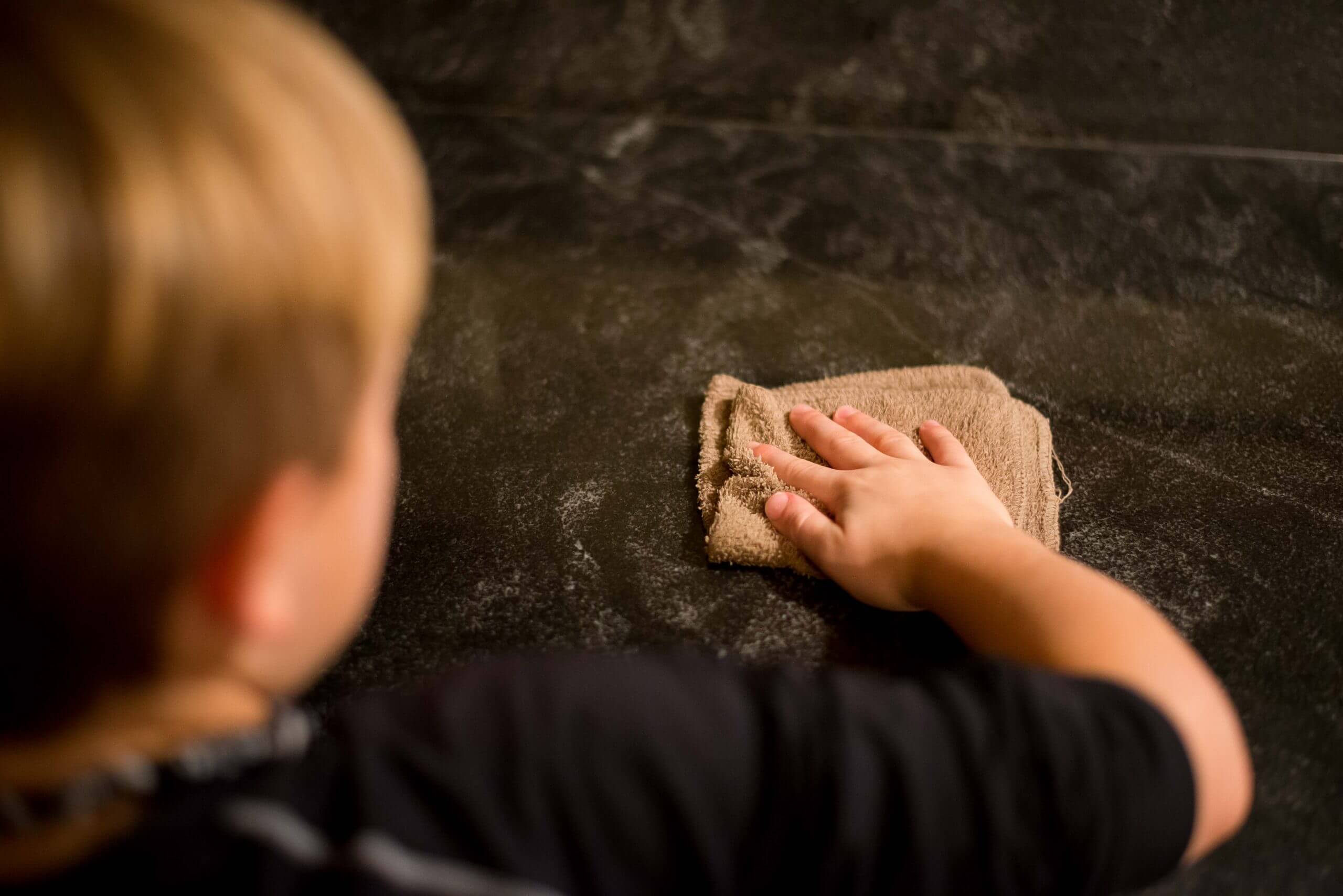 A child washes a hard surface with a rag.