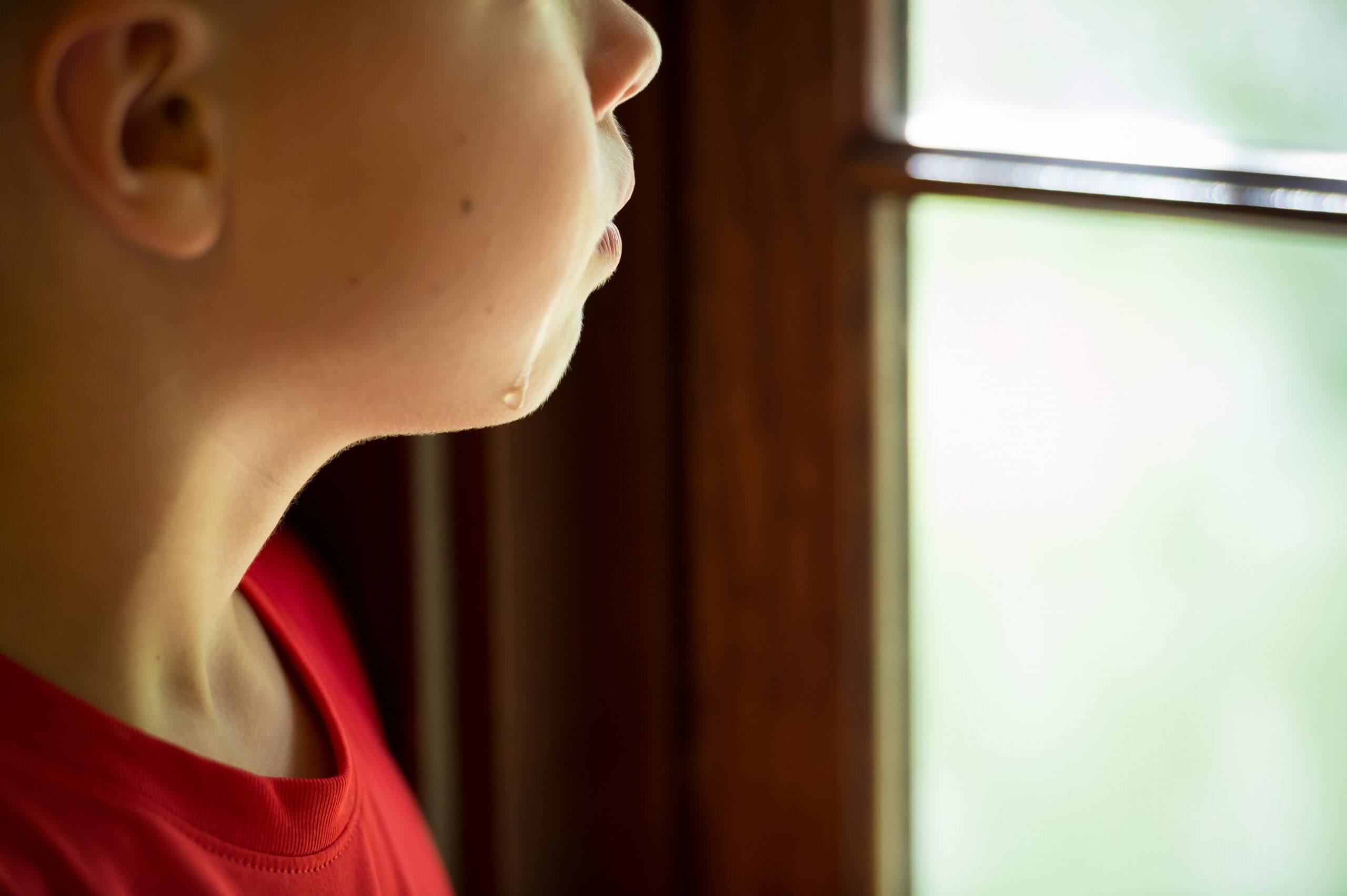 A focused view of a boy's face as he looks out the window. A single tear falls down his face.