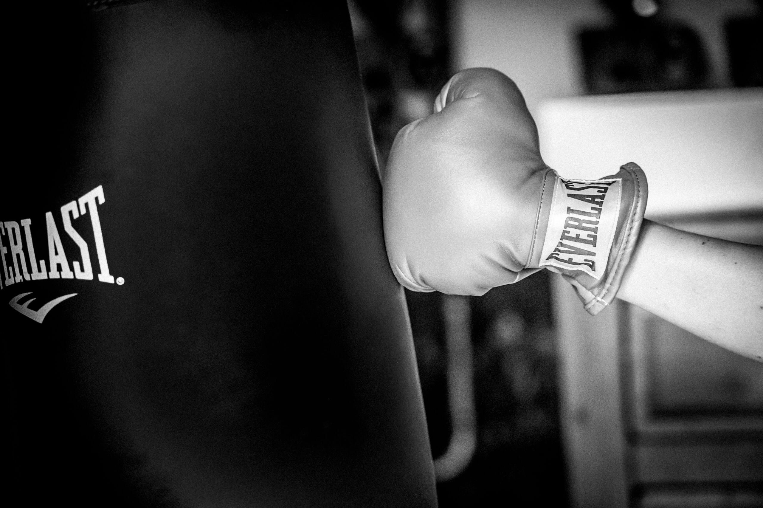 A person's fist wearing an Everlast boxing glove punches a bag.