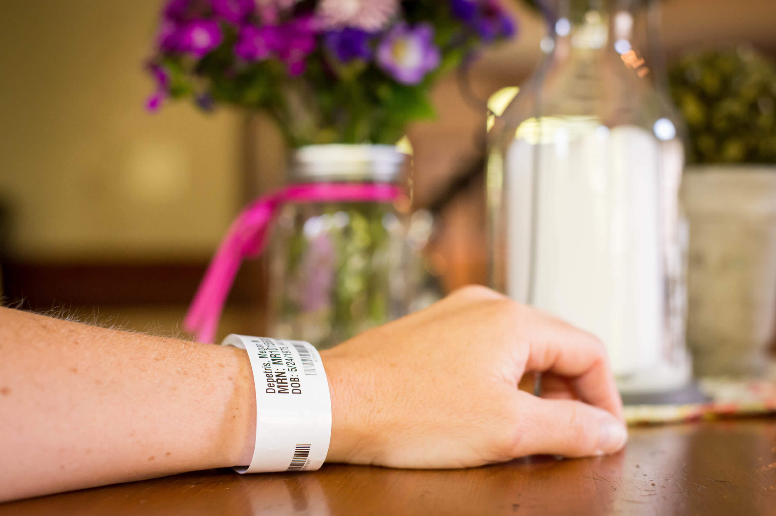 A focused view of an arm and hand on a table. On the wrist is a hospital identification bracelet.