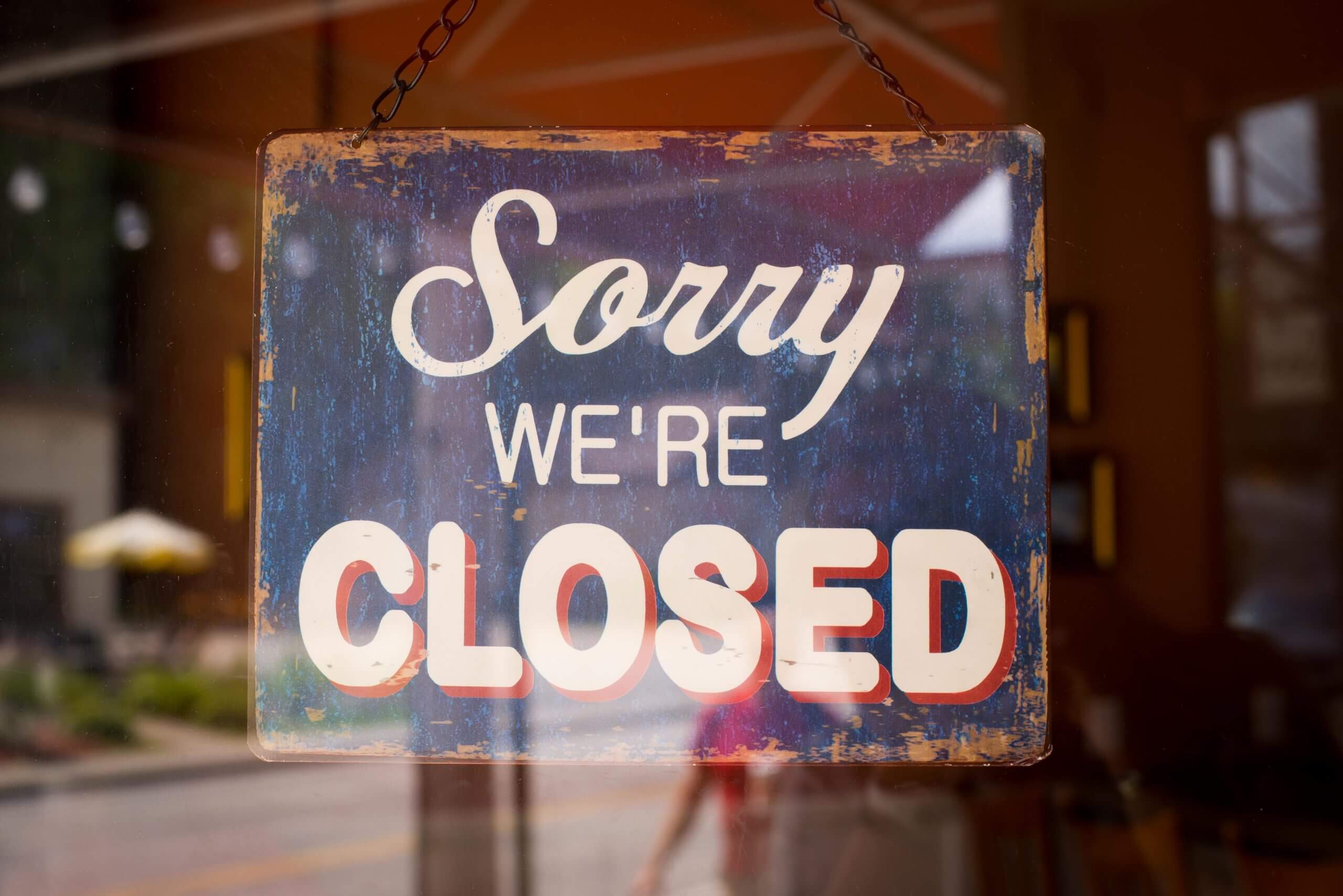 A view from the outside of a glass door looking in at a sign that reads "Sorry we're closed."