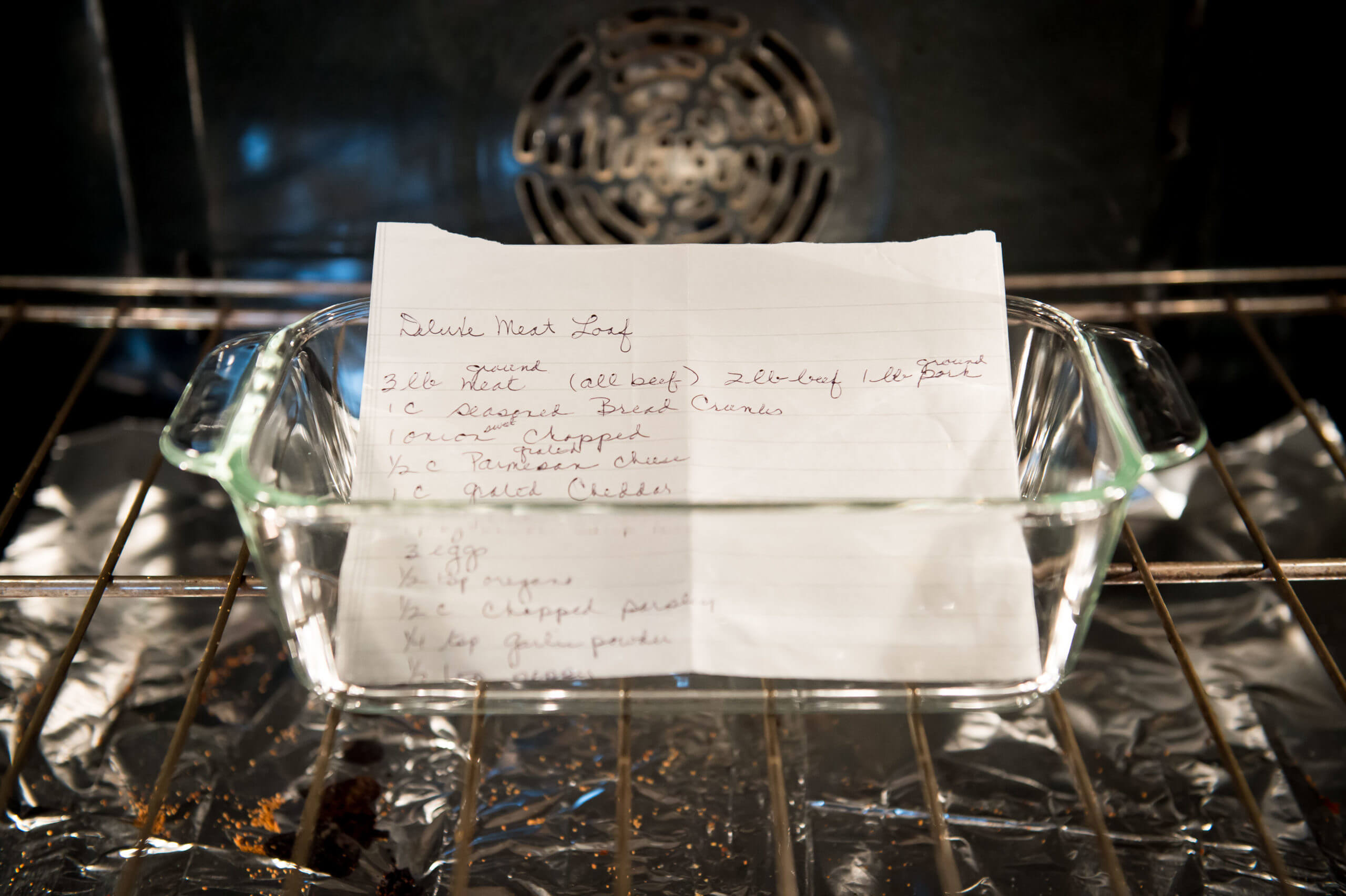 A glass dish with a recipe labeled, "Deluxe Meat Loaf" is inside of an oven.