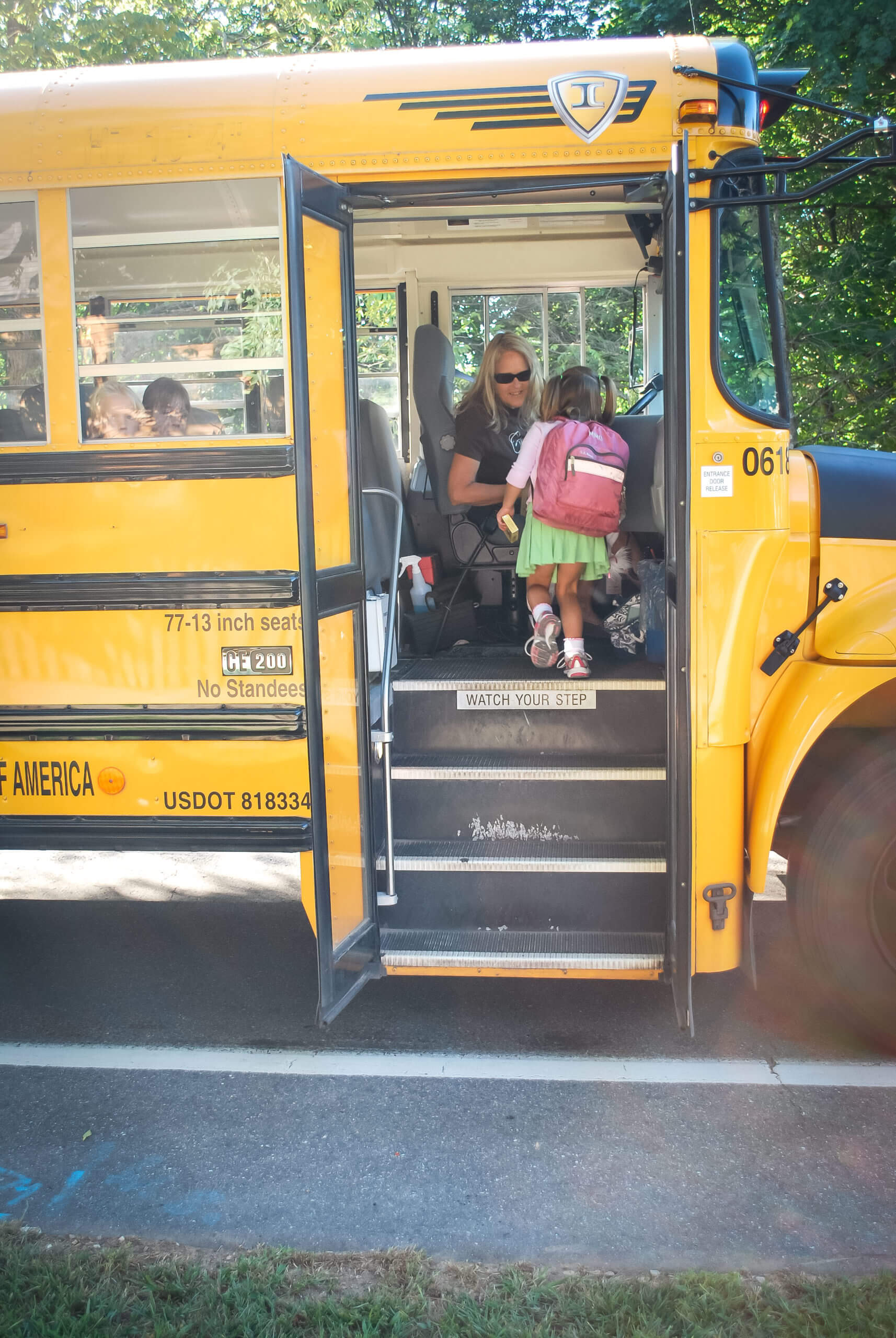 A child walks up the stairs of a school bus. The bus driver greets the child.
