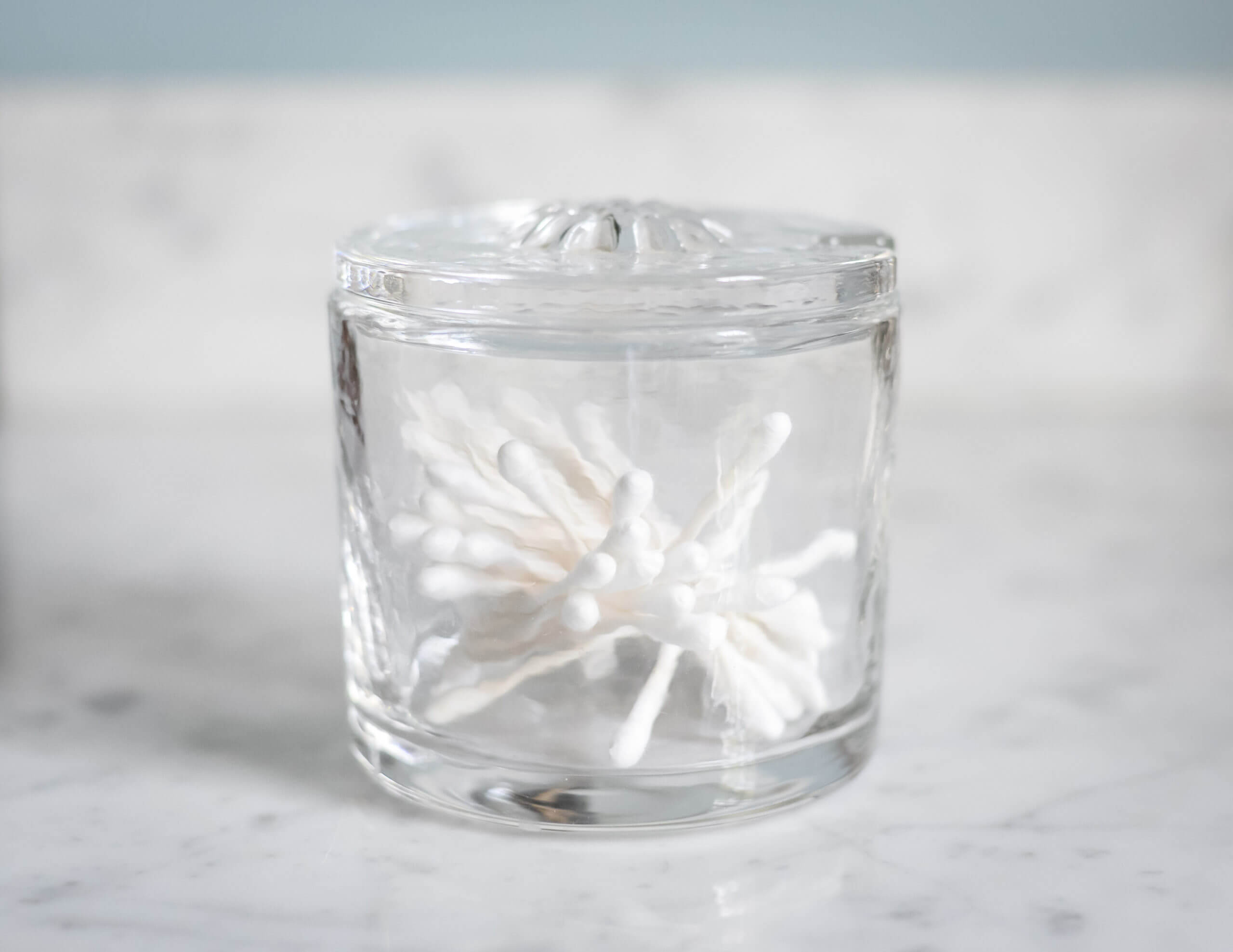 A glass container holds q tips.
