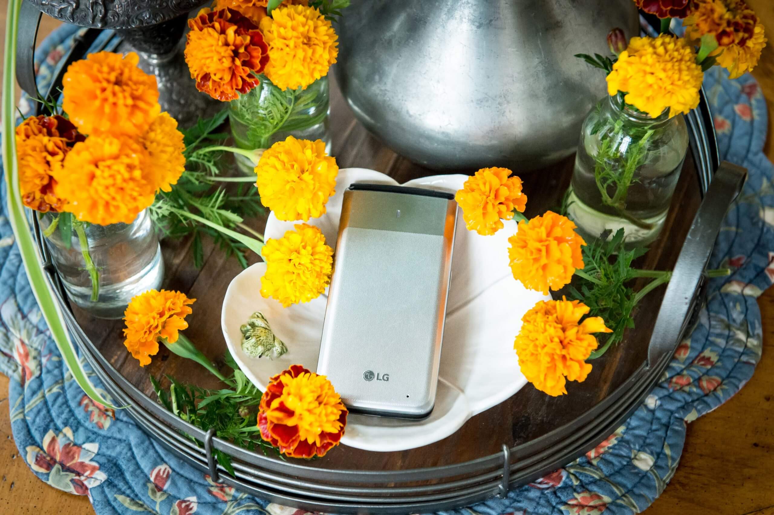 An LG flip phone on a coffee table tray. On the tray are vases of mums and cut mum stems surrounding the phone.