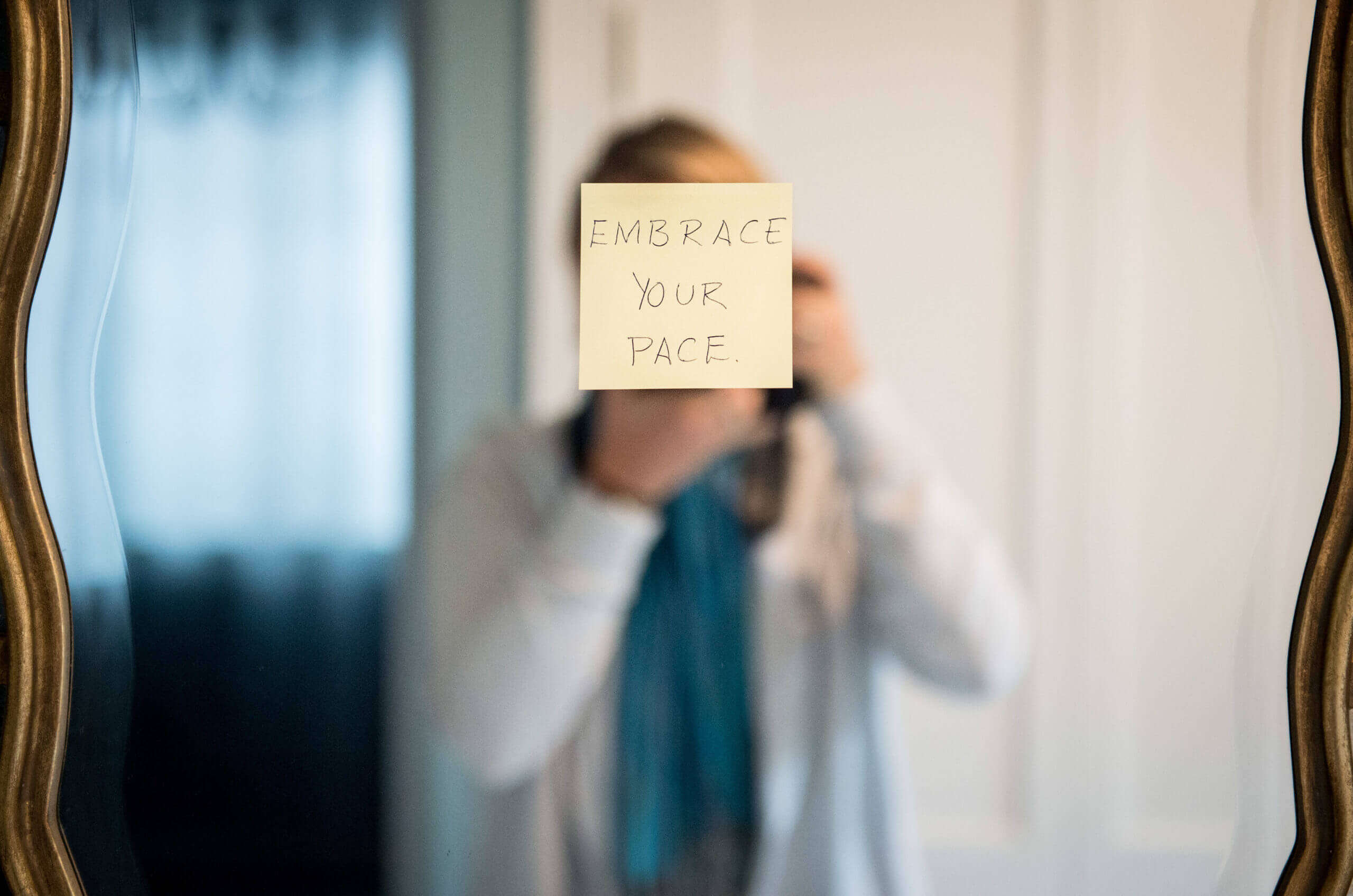 A sticky note on a mirror covers the face of the photographer taking the picture. The note reads, "embrace your pace."