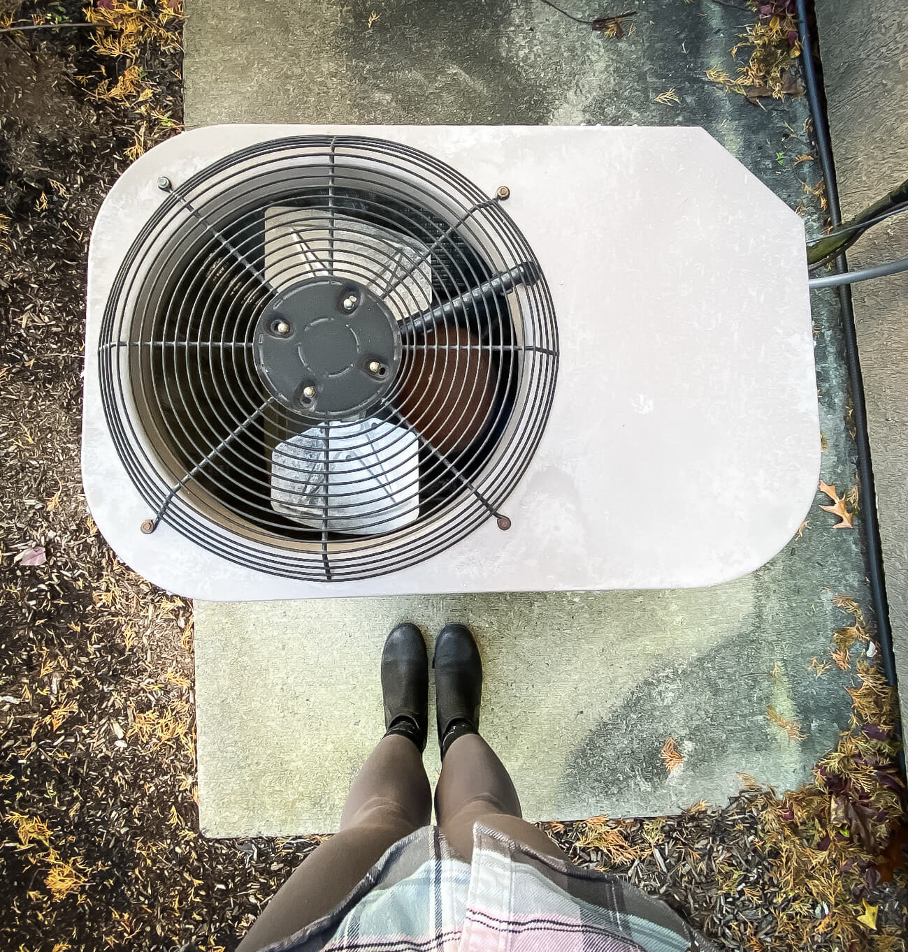 A view looking down at a central air conditioning fan. The photographer's legs and feet are shown.
