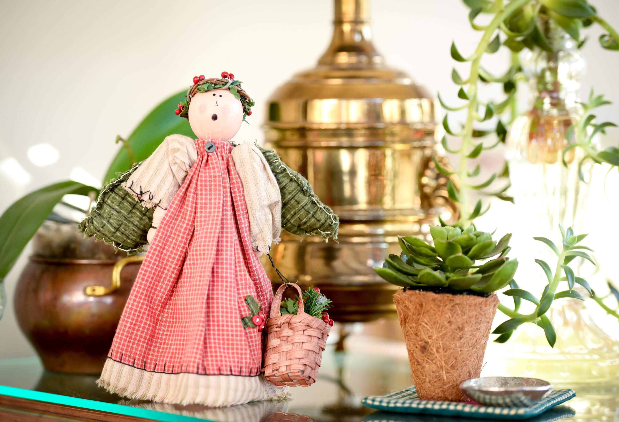A singing Christmas angel ornament stands on a table surrounded by several plants.