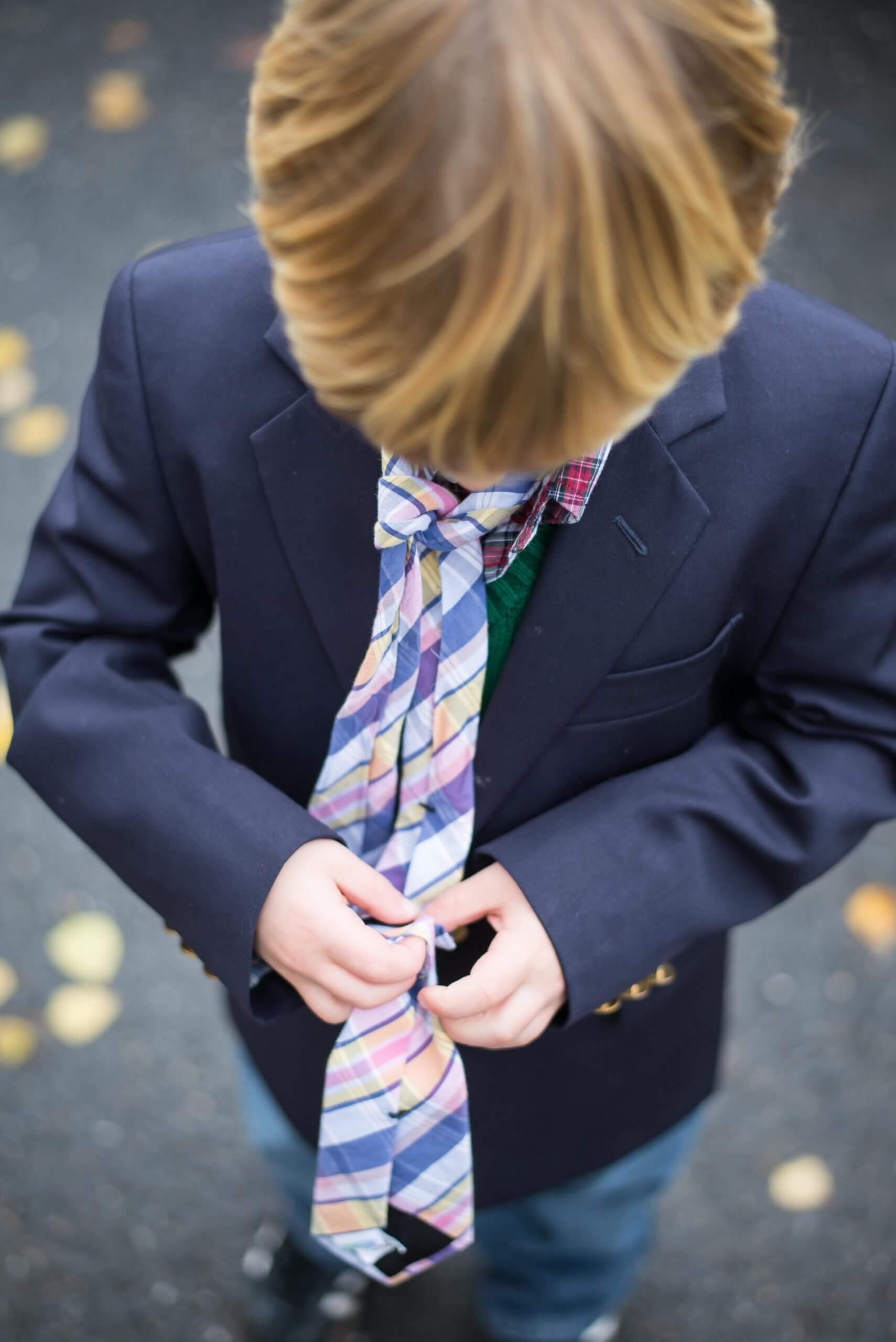 A view looking down over a child holding the tail of a tie loosely tied around his neck.