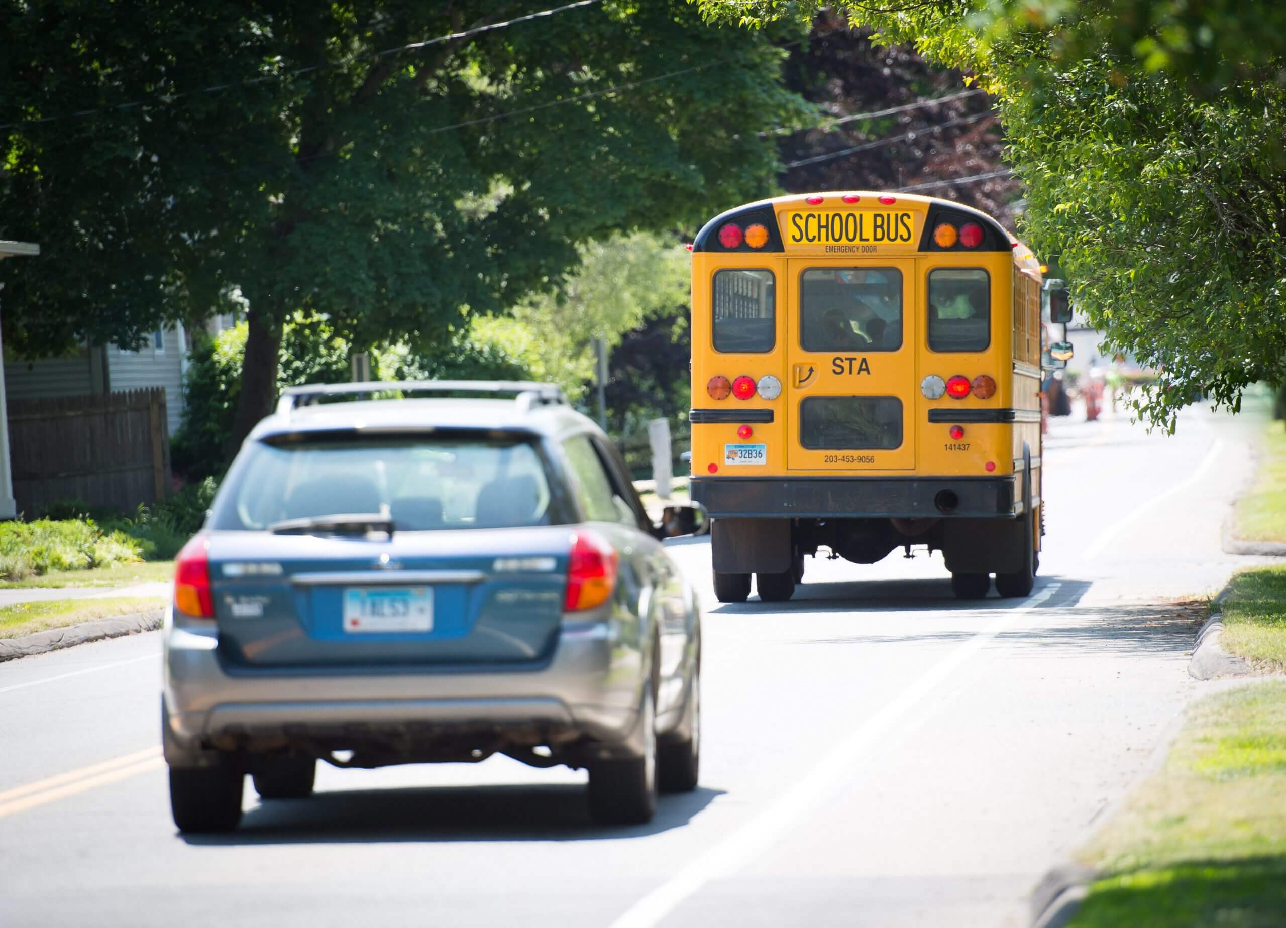 A school bus travels down the street followed by a car.