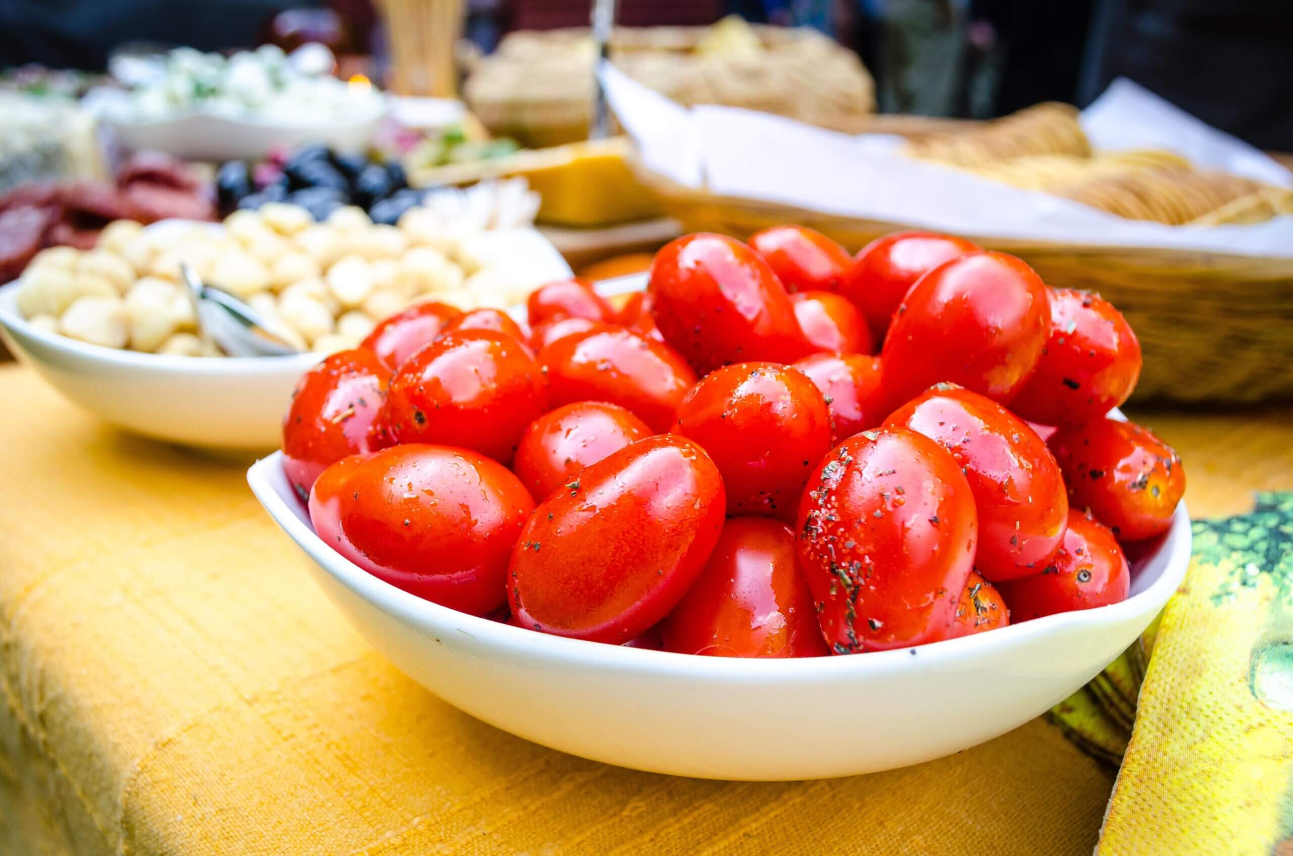 A bowl of cherry tomatoes on a table beside other bowls of food.