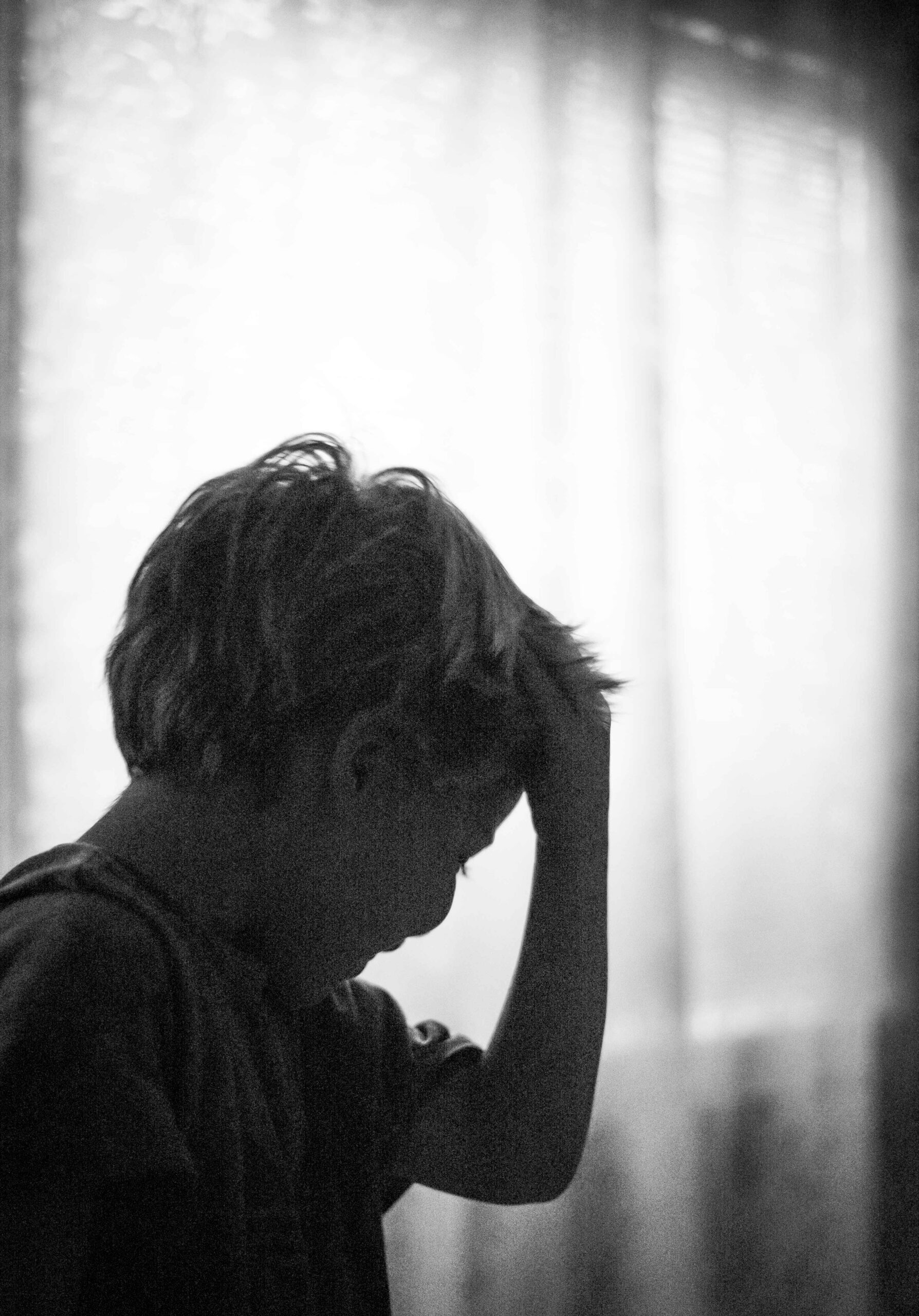 The profile of a young boy. His forehead rests in his hand, his fingers press his hair back, and his eyes are closed.