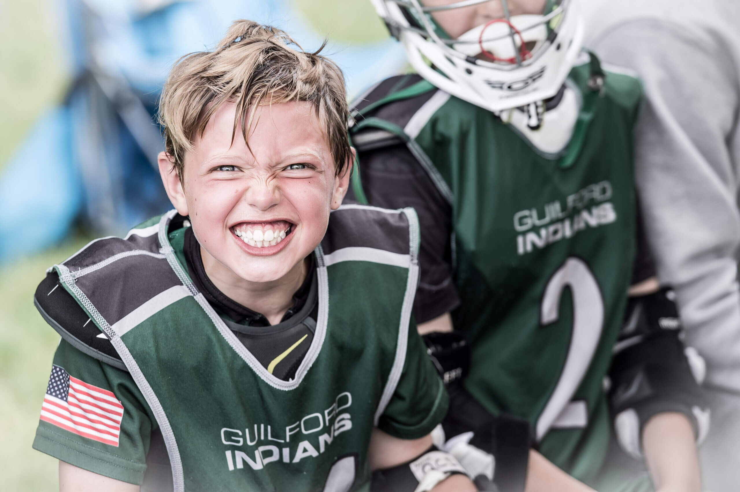 A child in a sports jersey smiles widely and scrunches their nose.