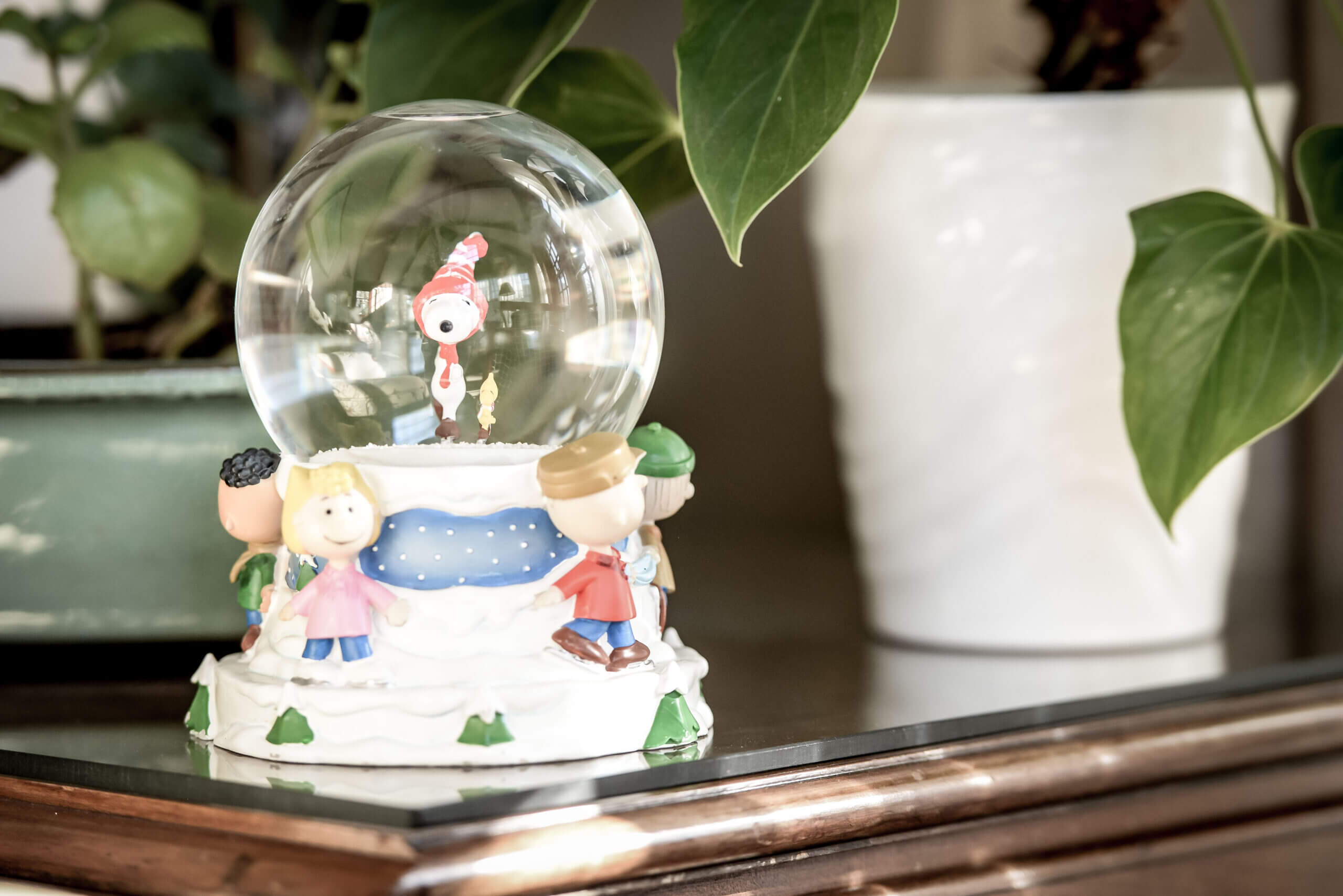 Snoopy snow globe sitting on a table with some plants behind it