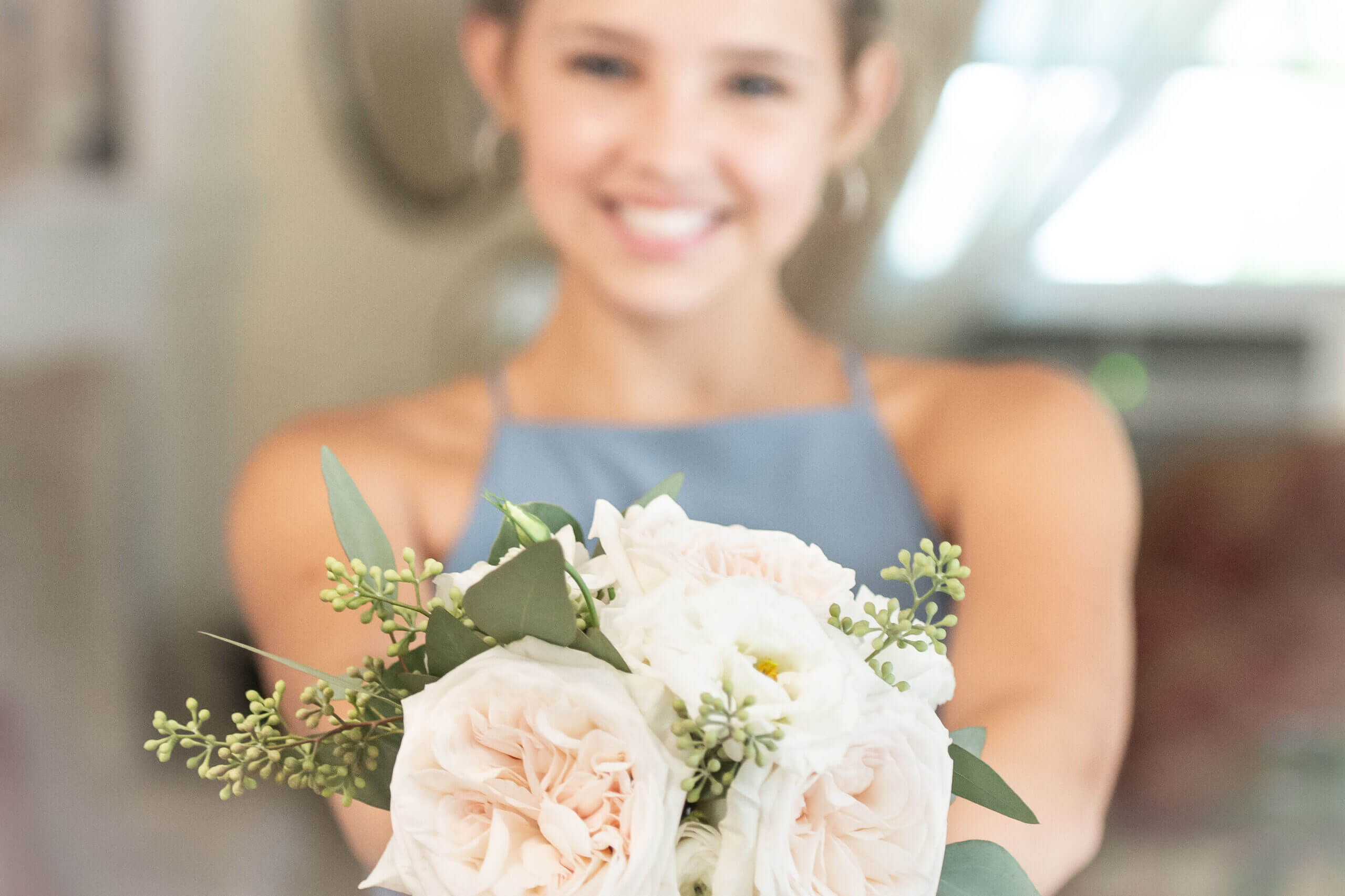 Female teenage girl out of focus holding a bouquet of flowers that are in focus, out in front of her.