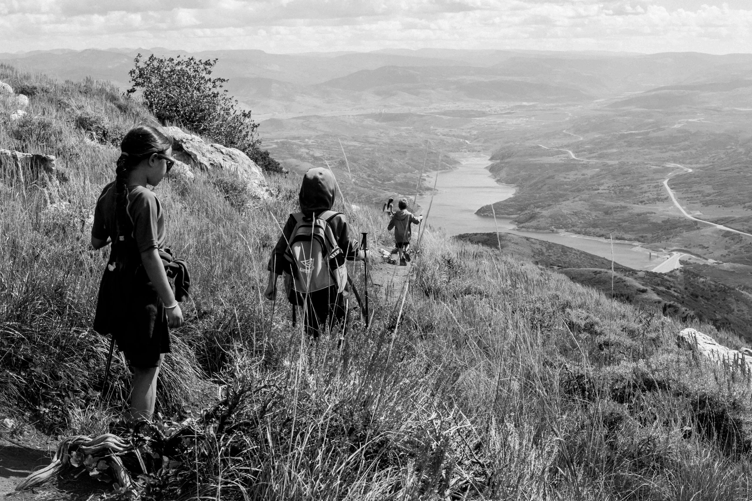 Black and white image of a big sky and Utah mountains in the background and four kids walking down a mountain trail.