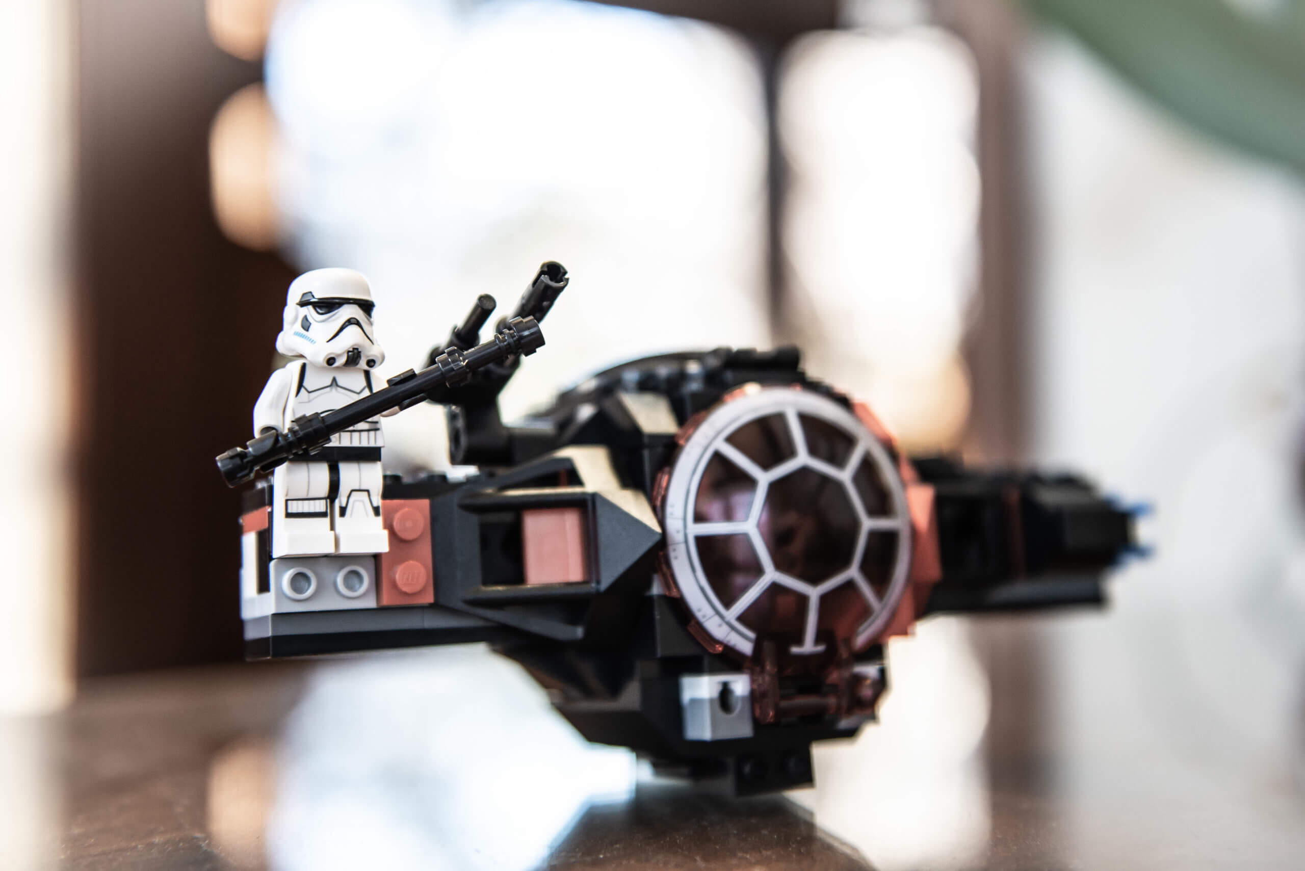 Color image of a Lego Star Wars stormtrooper sitting on the wing of a black Lego TIE fighter spaceship.