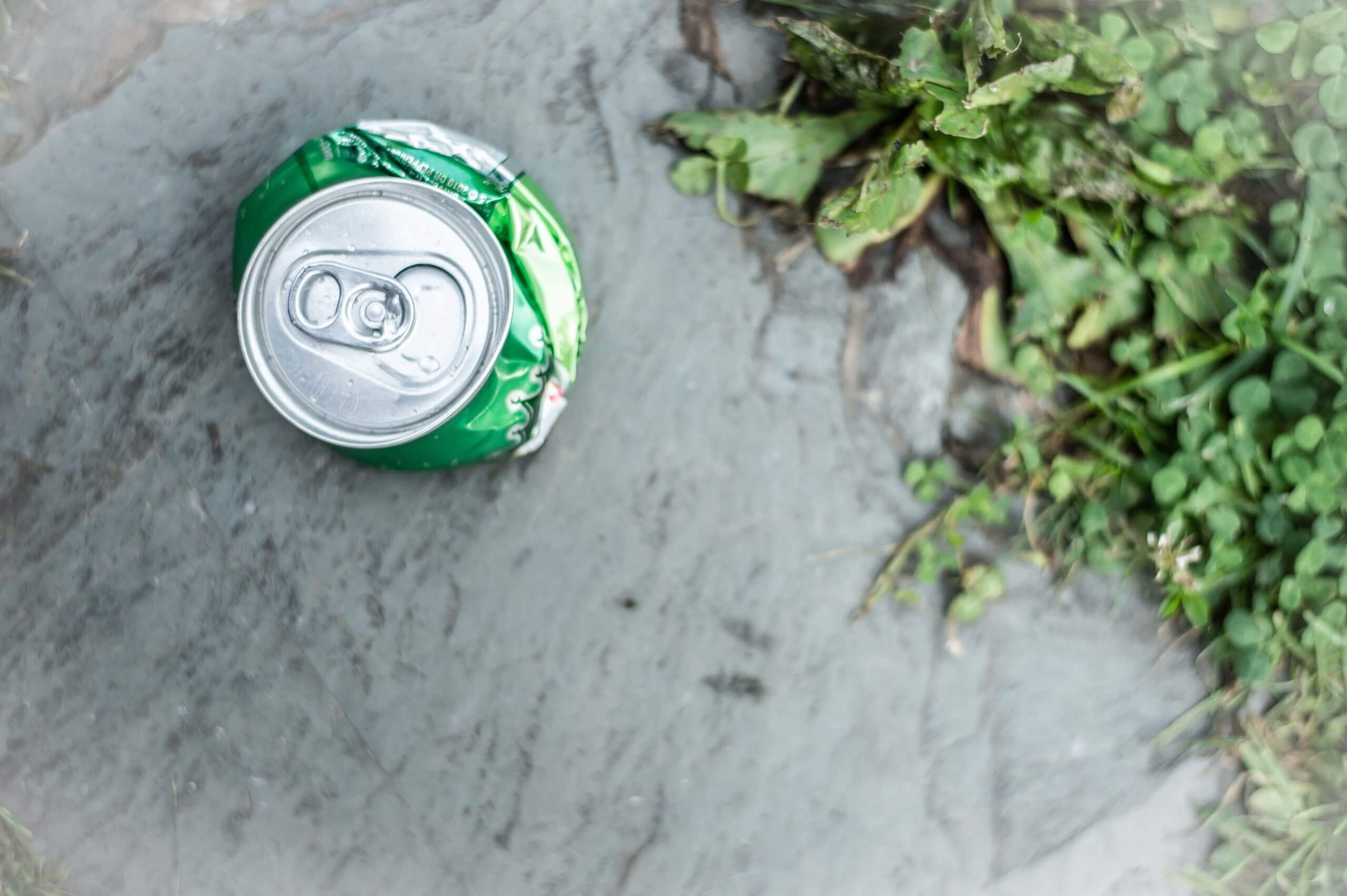 Color photo close-up of a crushed aluminum ginger ale can on a walkway outside.