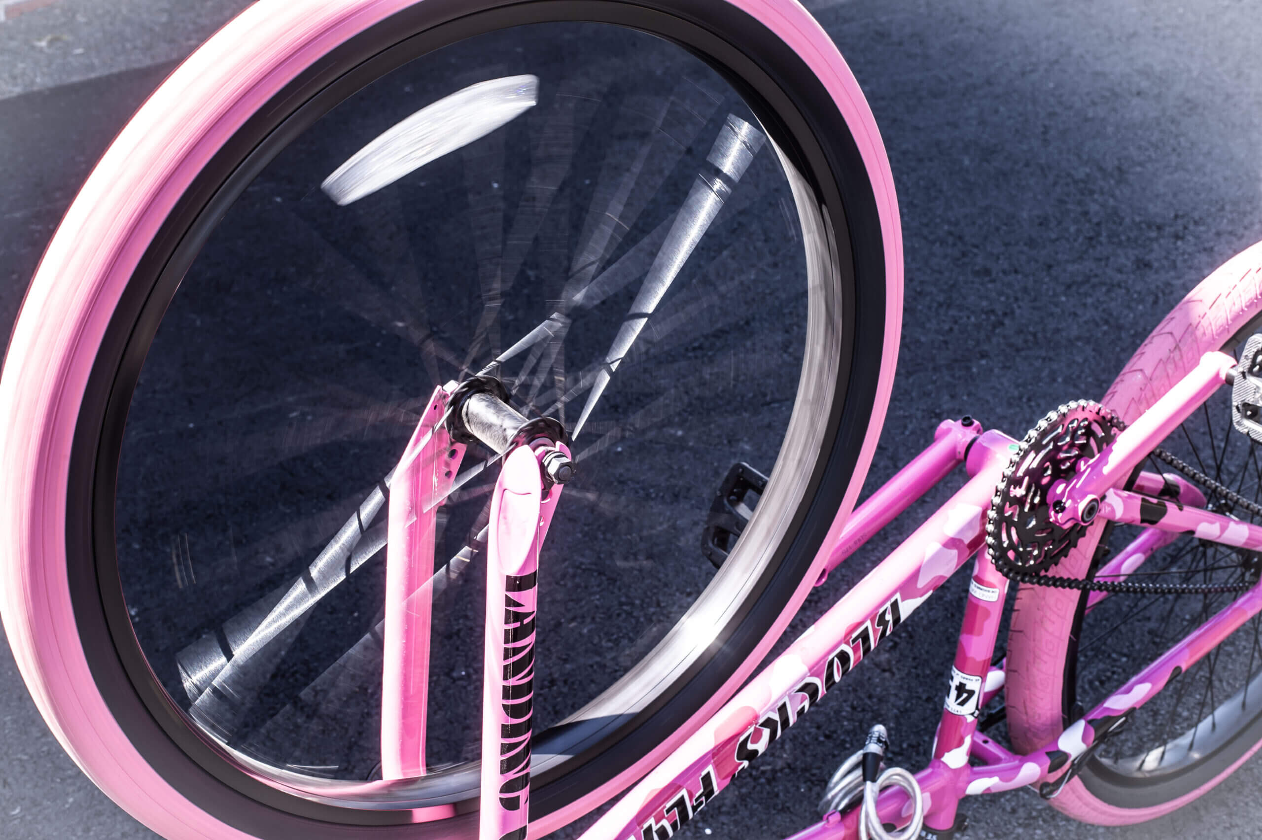 Color image of a pink bike upside-down on black pavement. The front wheel is in motion.