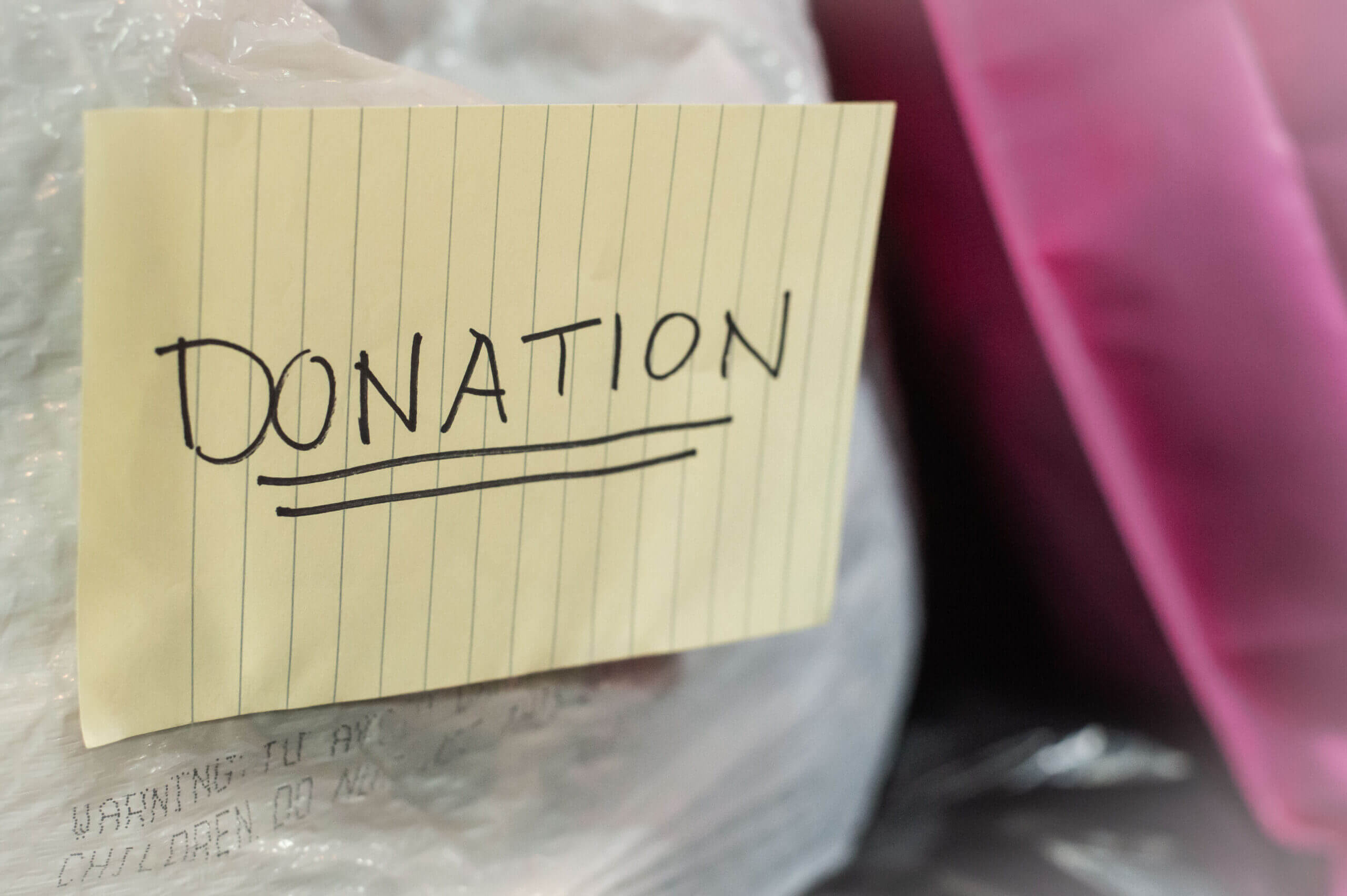 Color image with a few garbage bags piled up on top of each other. The focus of the photo is a sign on one of the bags that reads, "DONATION"