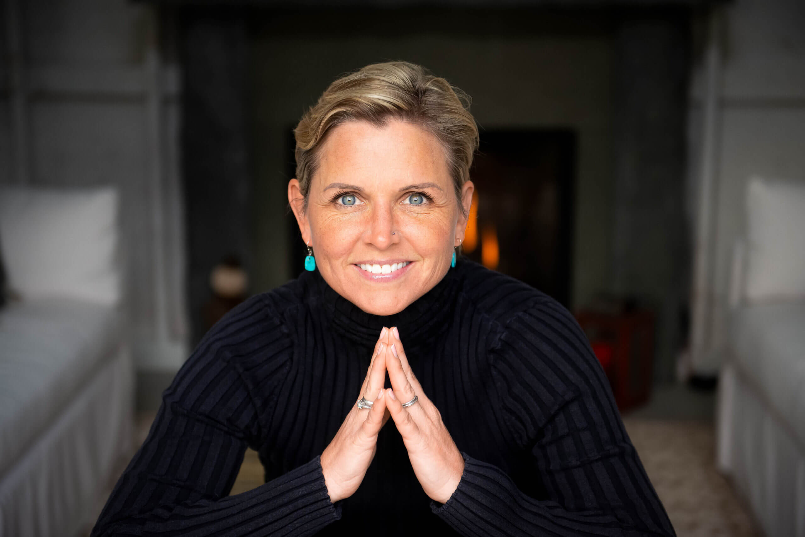 Color image of a white woman with blond hair in a black turtleneck looking right into the camera smiling.