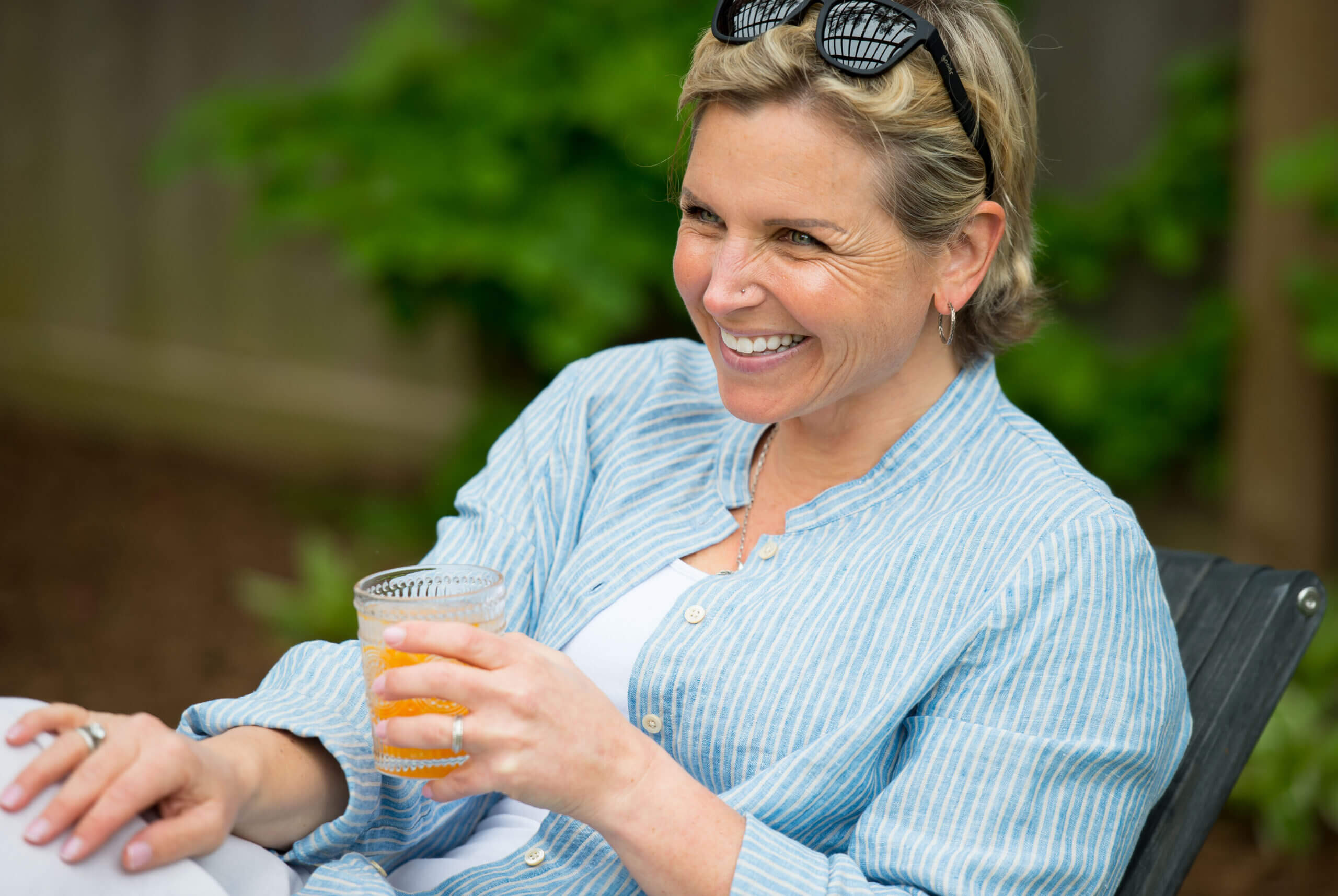 Color image of a while woman with short blond hair sitting with a smile and a glass in her left hand.