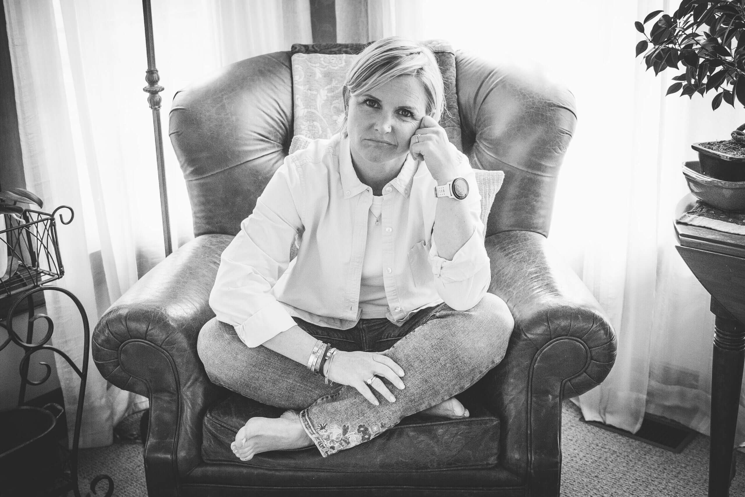 Black and white image of a white 40-something year old woman sitting in a big leather chair with a disgruntled look on her face.