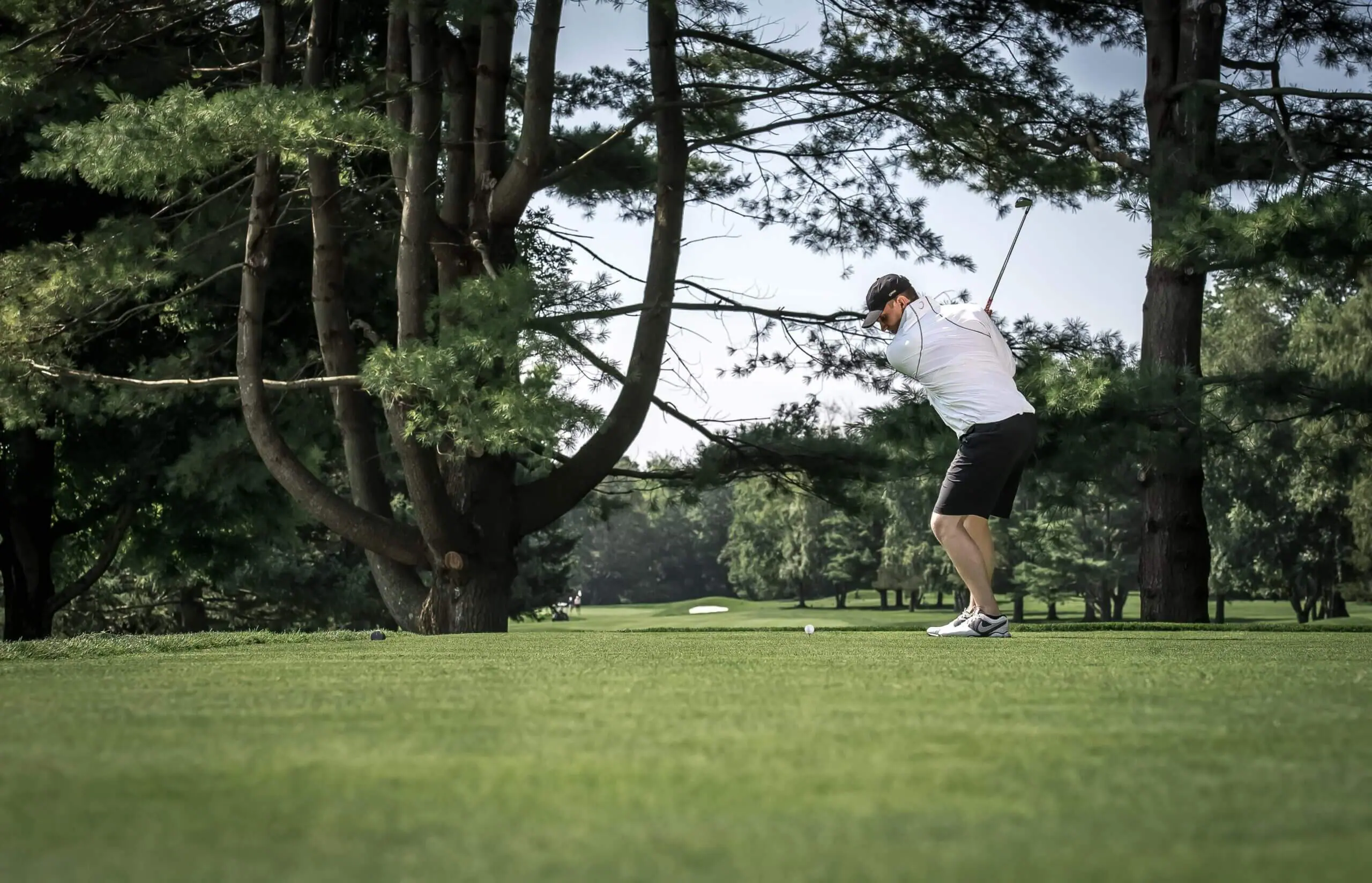 Color image of a white man in his back swing on a golf course.