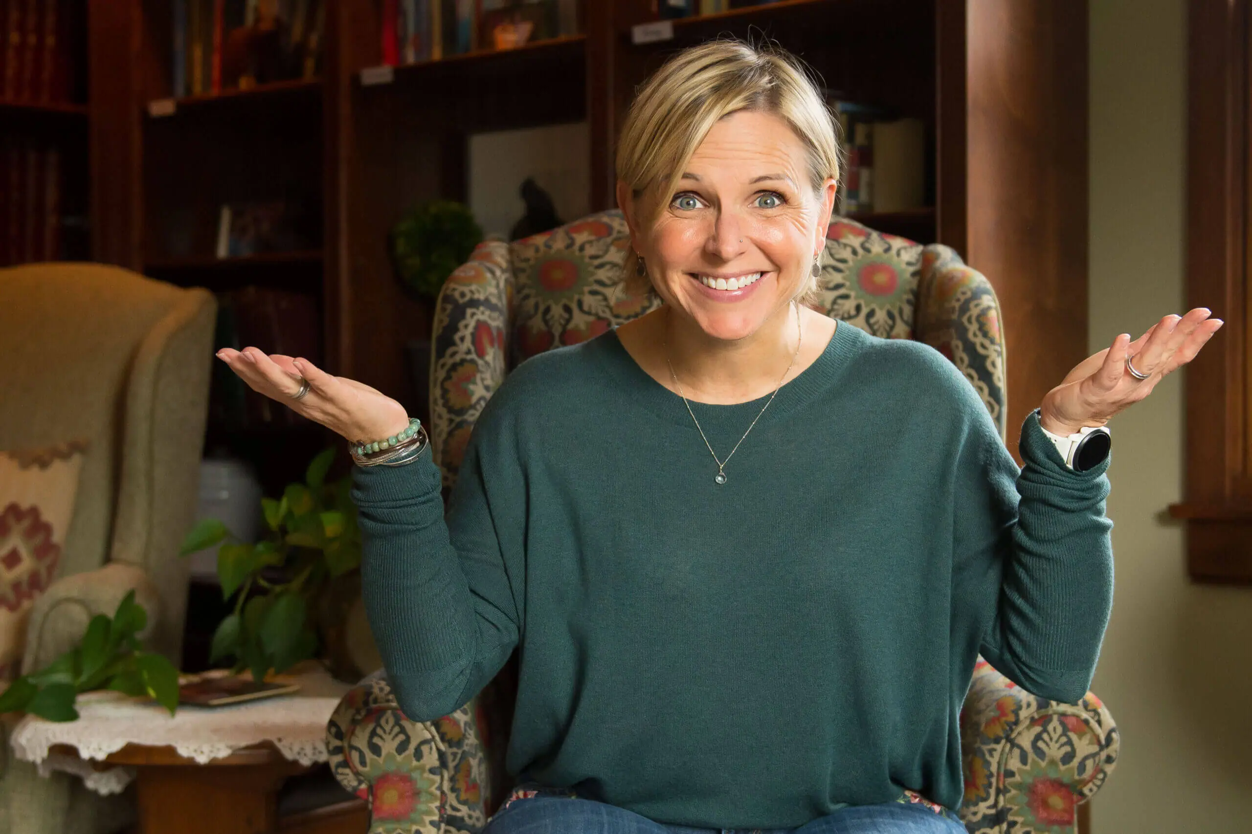 White middle aged woman with her hands up in question and a smile on her face.