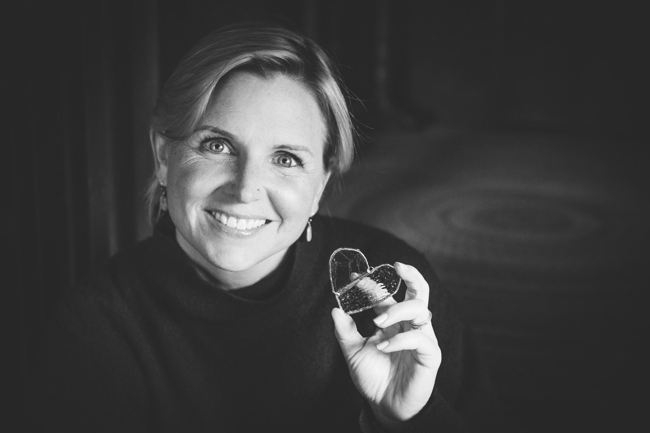 Black and white photo of a 40-something holding a glass heart in her left hand.