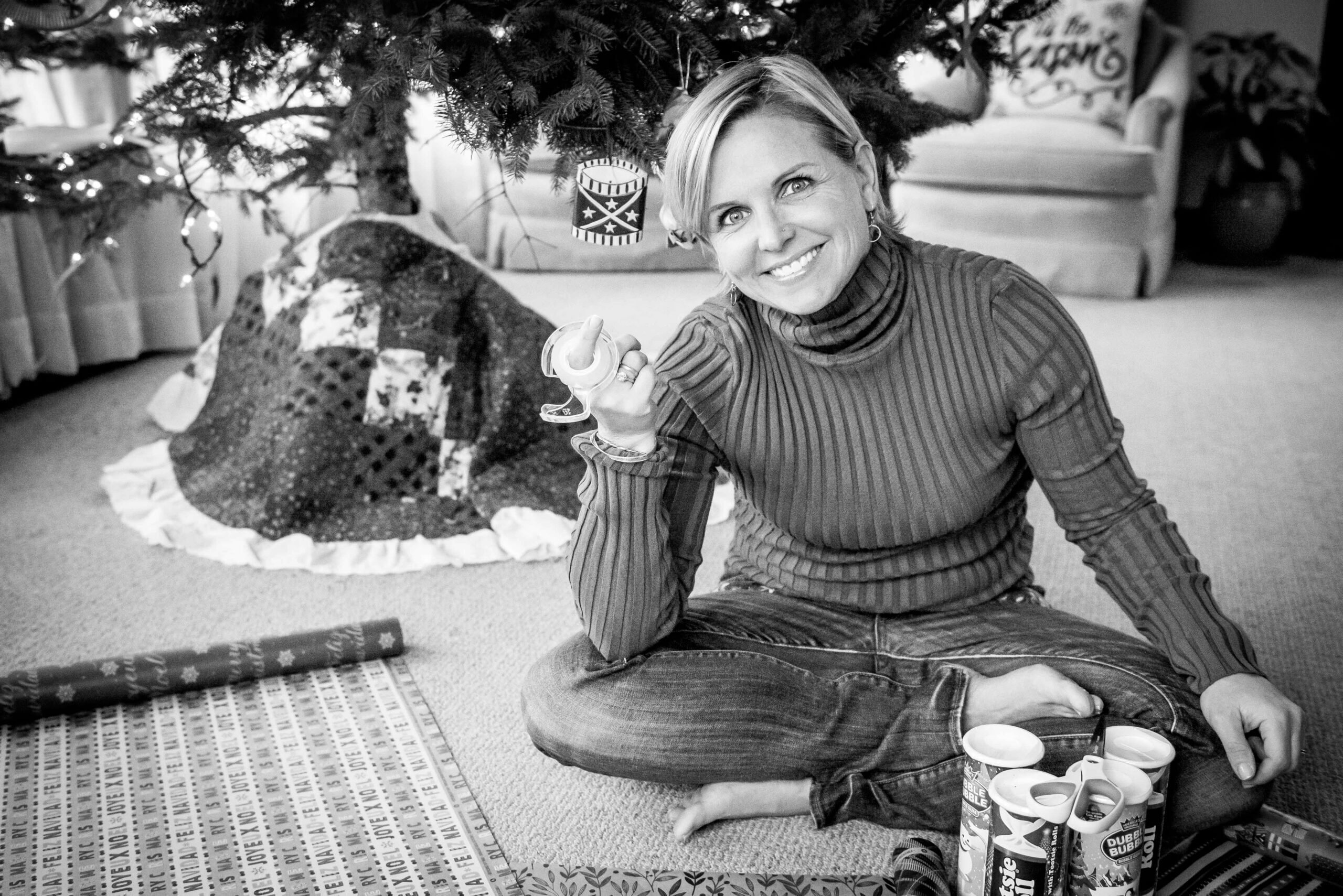 Black and white image of white woman sitting on the floor wrapping Christmas presents.