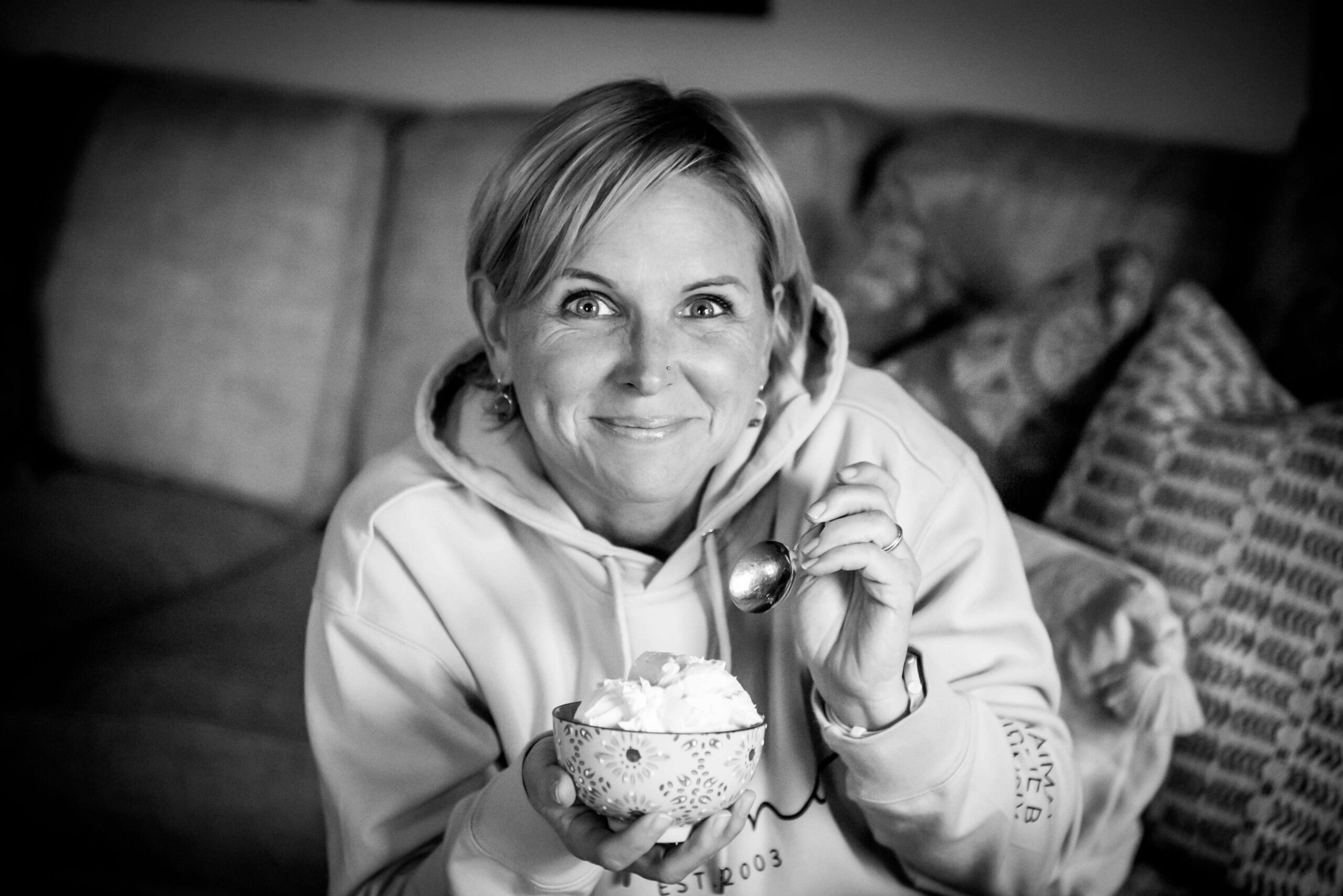 Black and white image of a white woman eating ice cream out of a bowl.