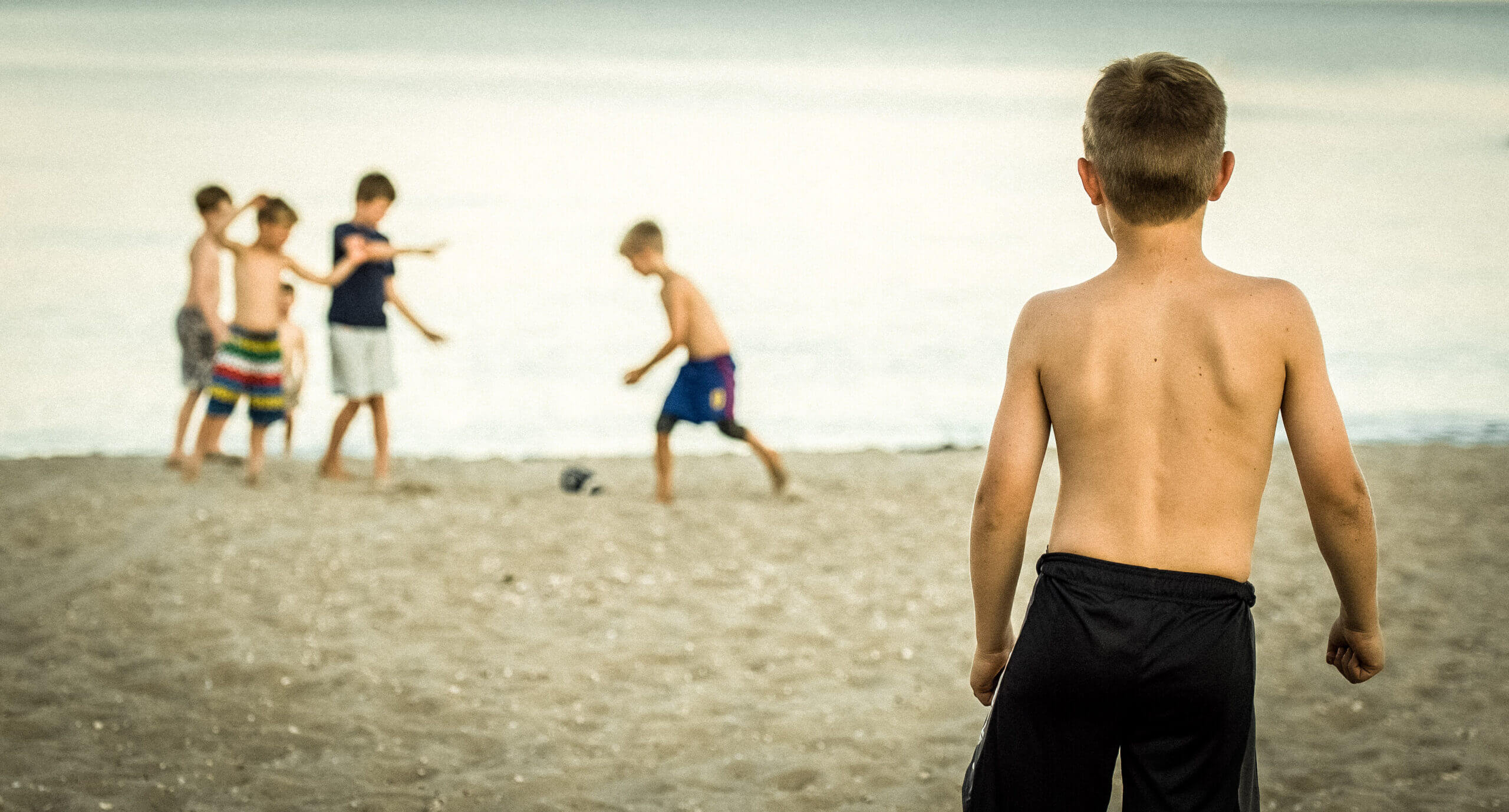 Color image of the back of a little boy on the beach throwing a football to other boys who didn't catch it.