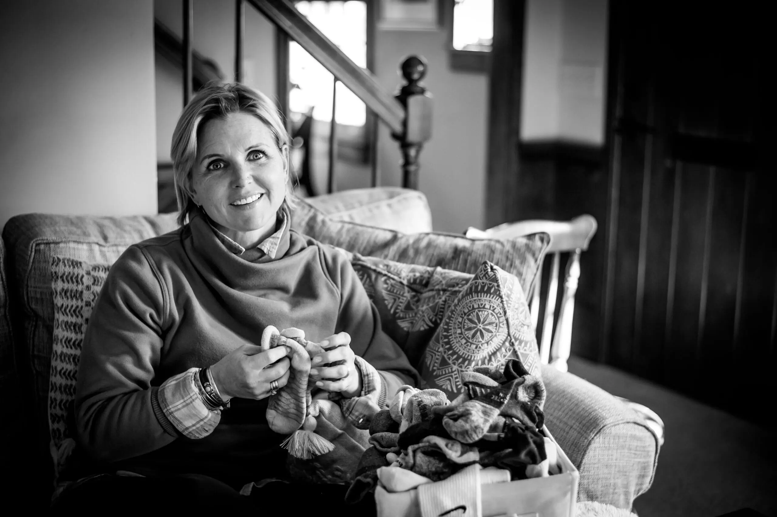 Black and white image of a white woman on a couch folding socks while watching TV.