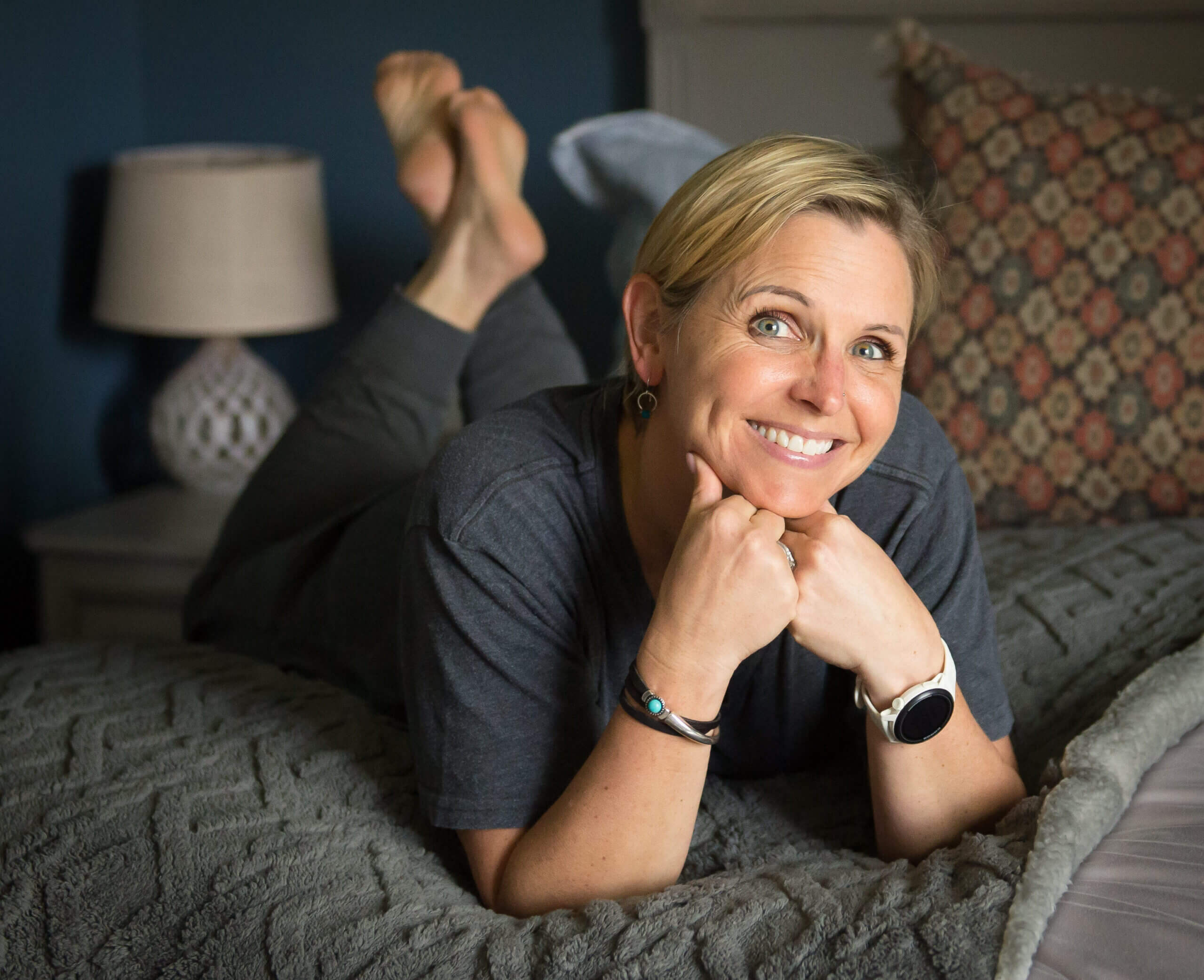 White woman lying on her stomach on a bed with her hands on her chin.