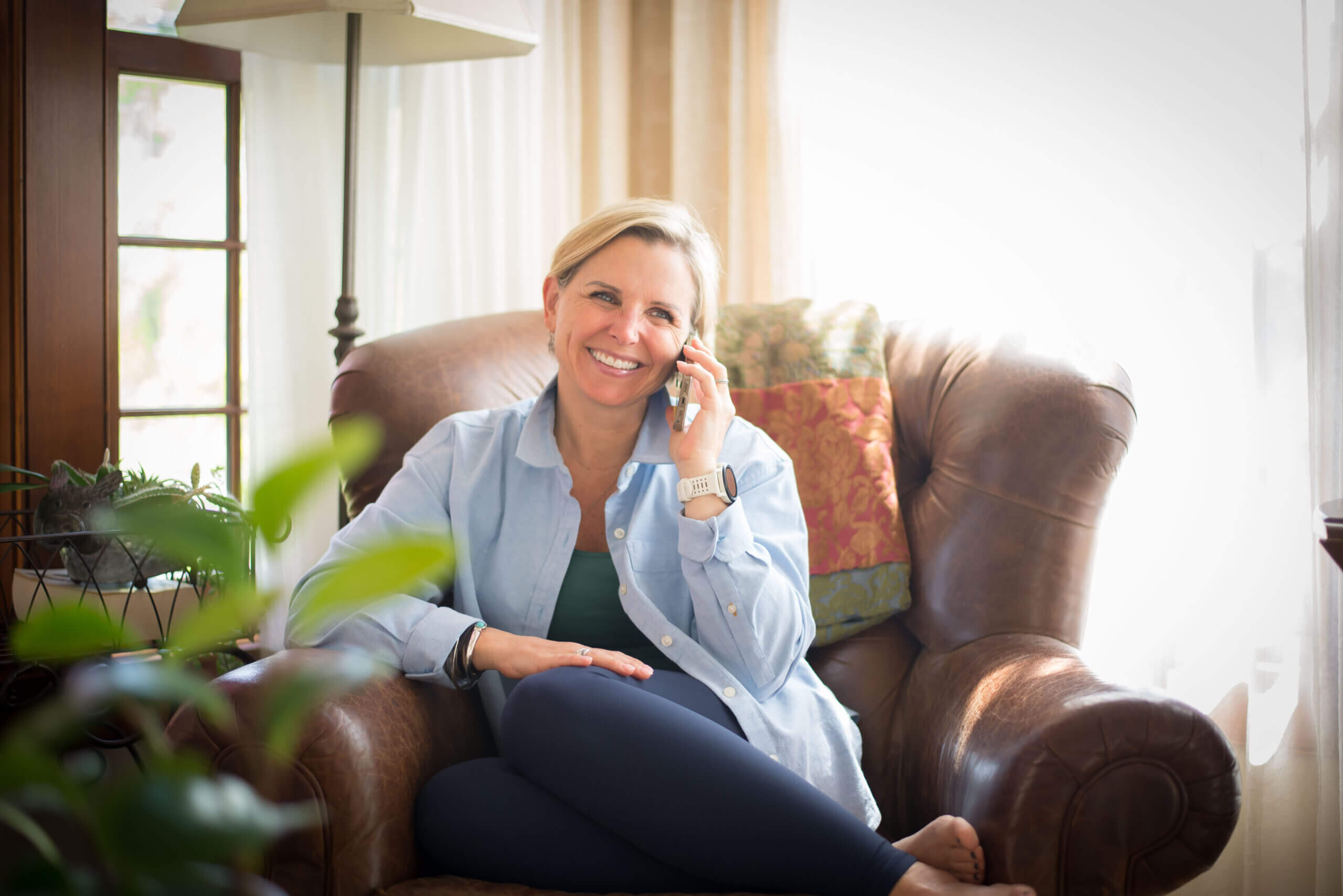 White middle aged woman in a leather chair on her cell phone.