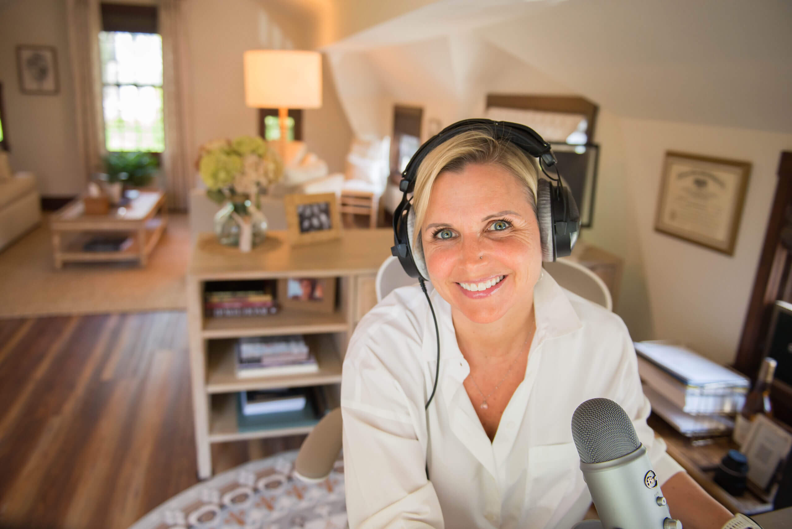 White middle aged woman at a computer with a microphone and headphones on.