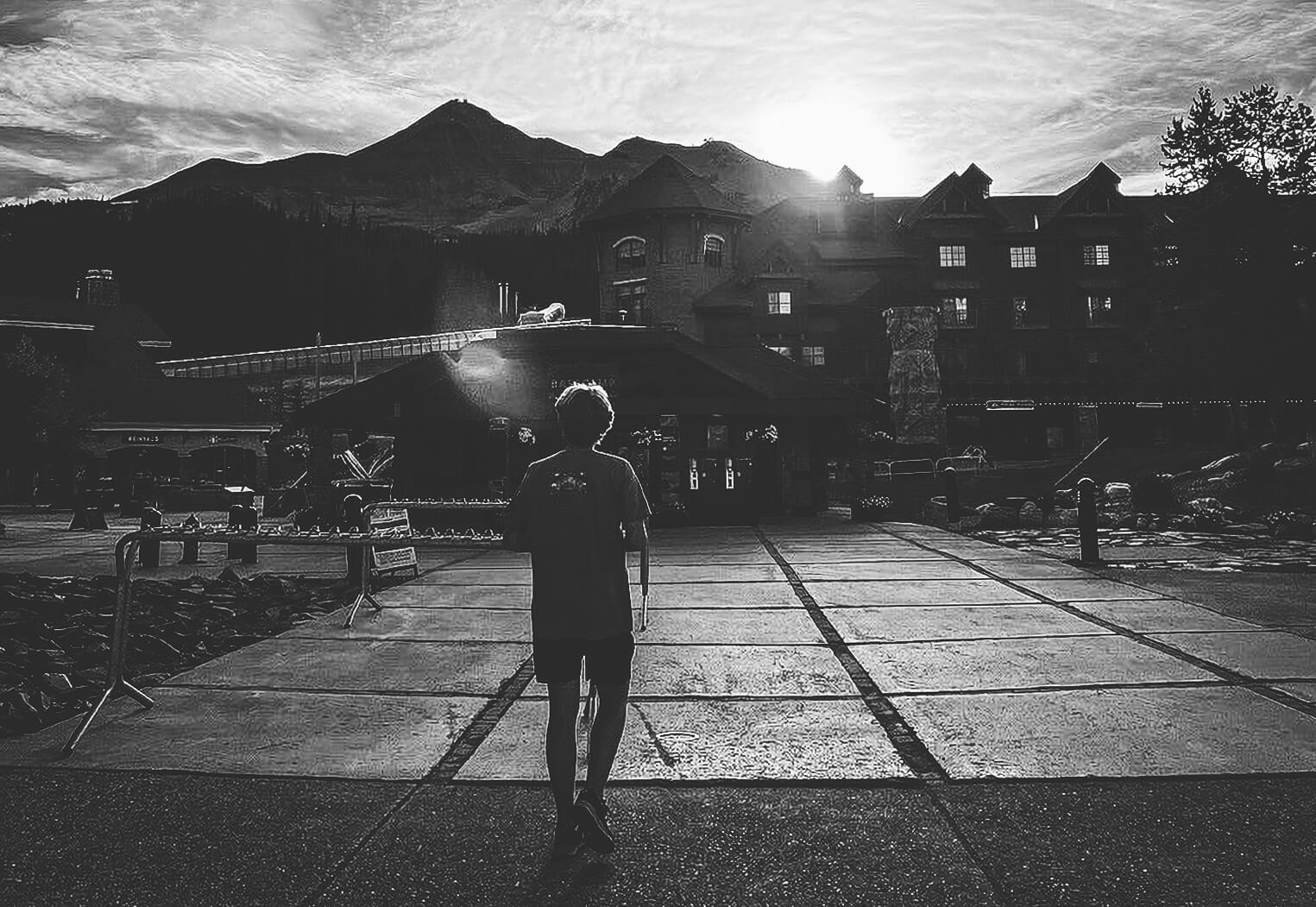 Dark black and white image of a tall white 18 year old walking towards a sun setting behind Big Sky mountain.