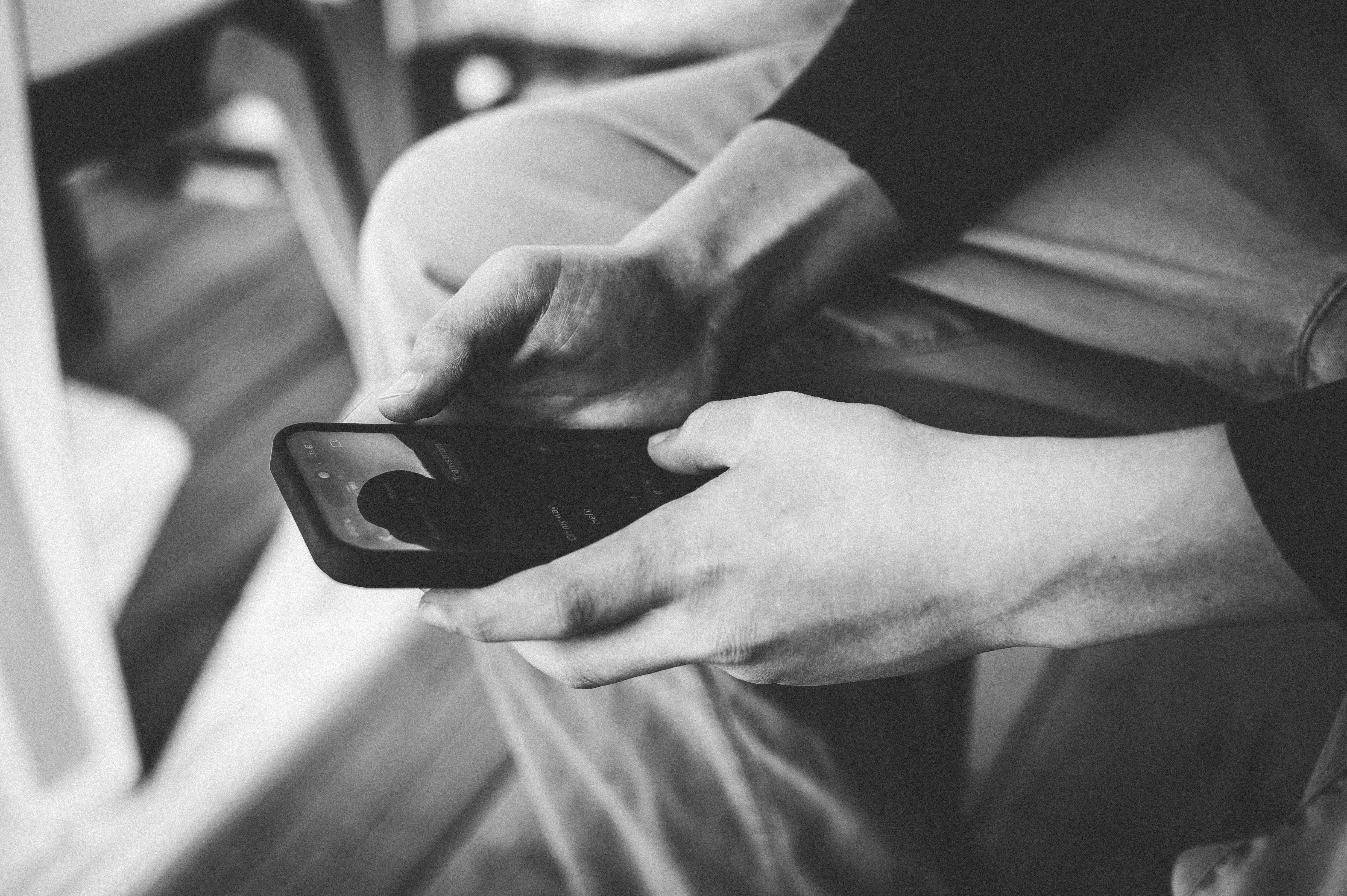 Black and white image of a sixteen year old white boy holding a phone. Only his hands and the phone are in view of the camera.